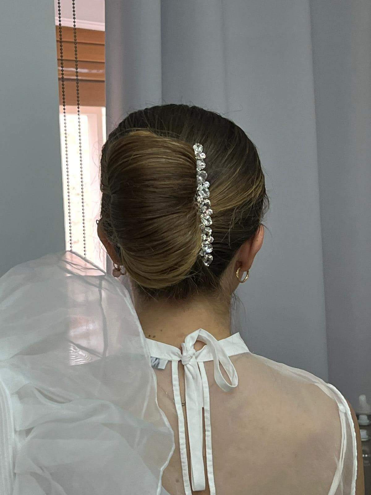 Donna con acconciatura raccolta, adornata con una forcina gioiello, che indossa un abito bianco.
