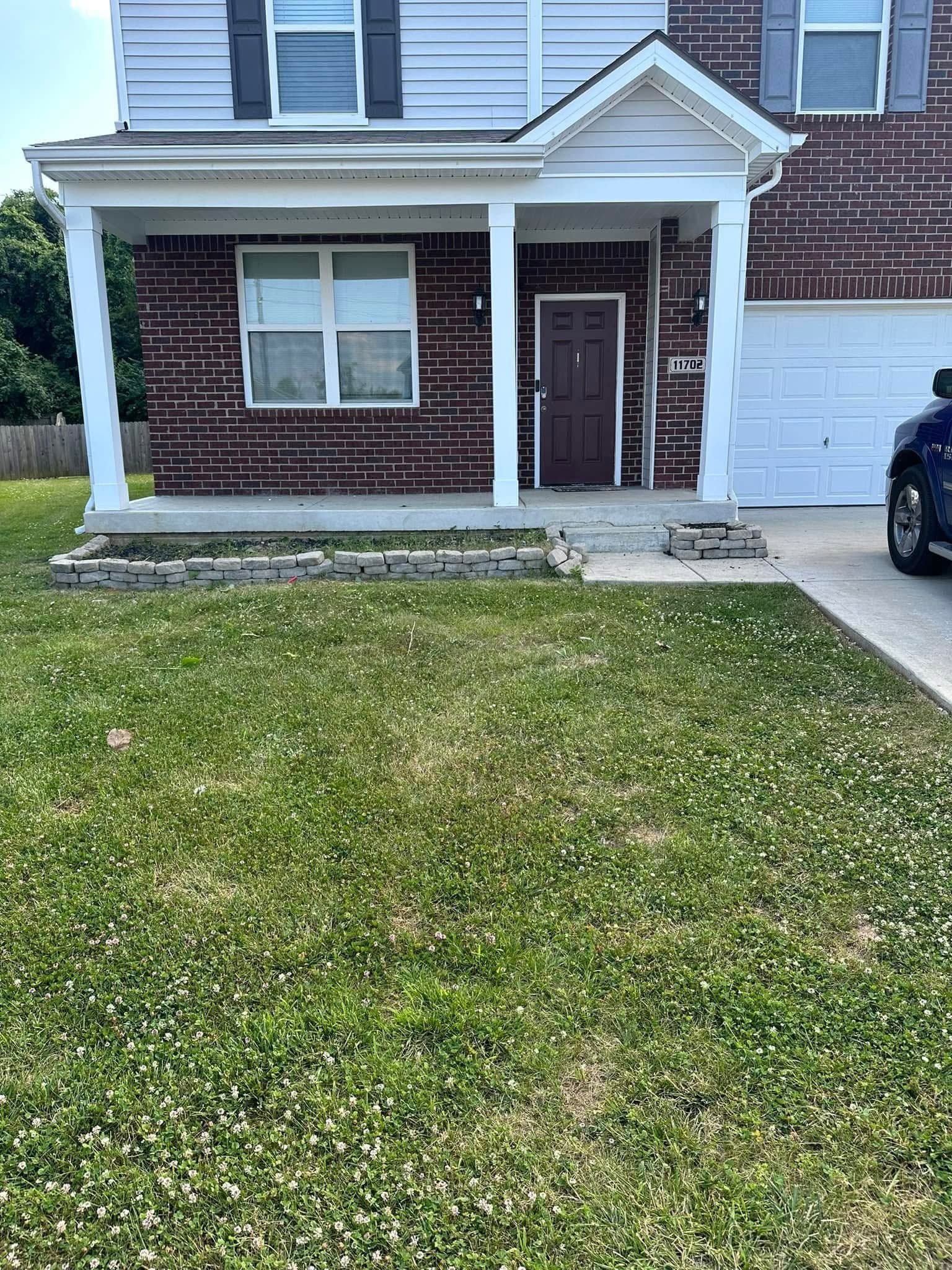 Front view of a suburban townhouse with a small porch, front lawn, and driveway beside a parked car.