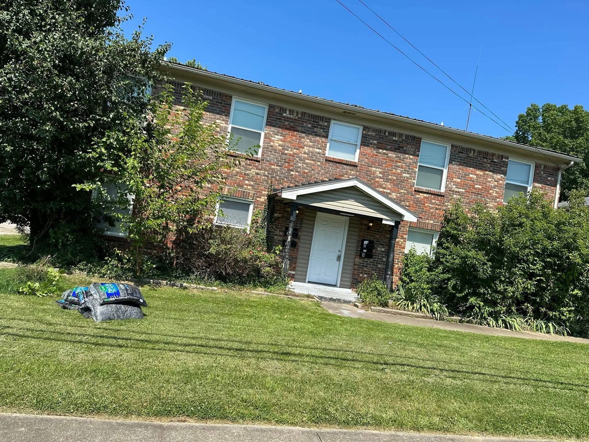 Two-story brick house with a front porch and lawn on a sunny day