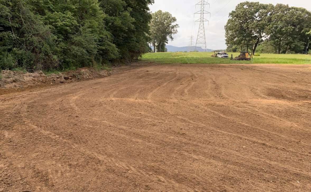 Freshly plowed brown field bordered by trees, with power lines in the distance.