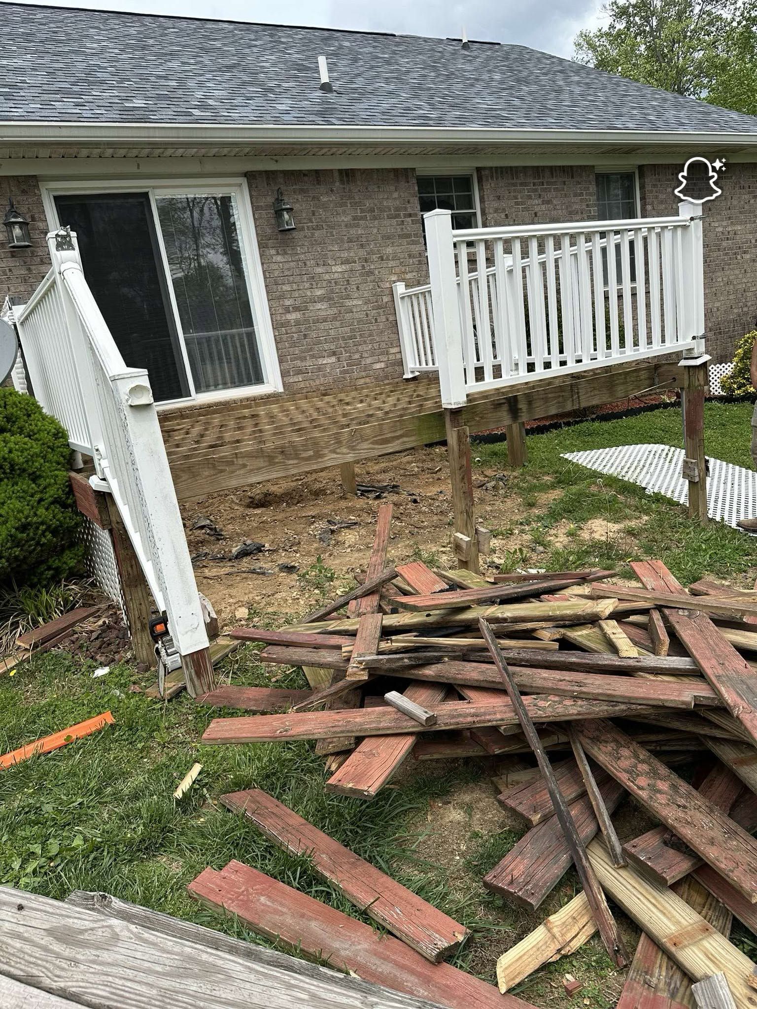 Damaged house deck with broken white railing and collapsed wood debris in the yard