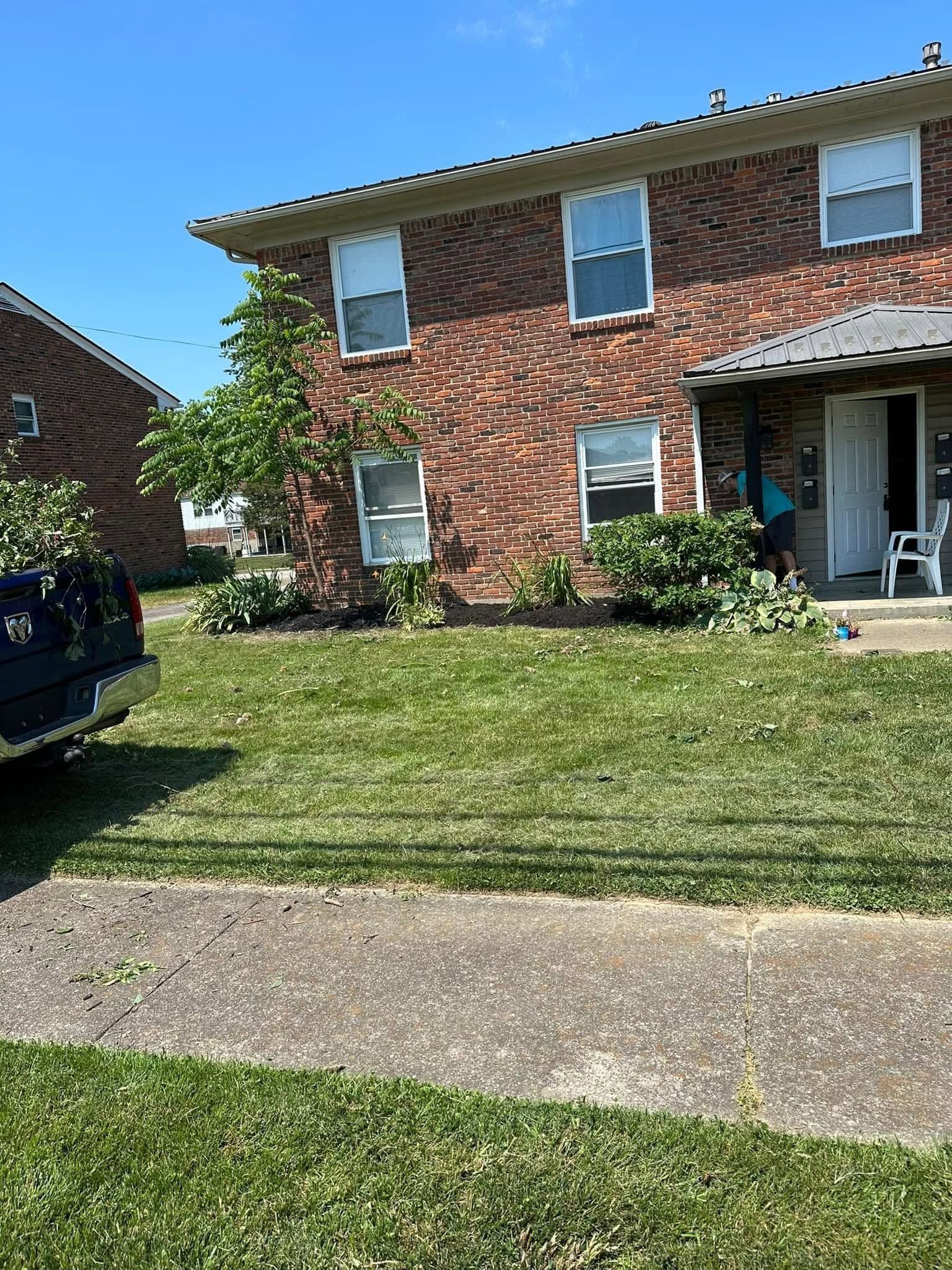 Brick two-story house with a front lawn, sidewalk, and a parked SUV on the left.