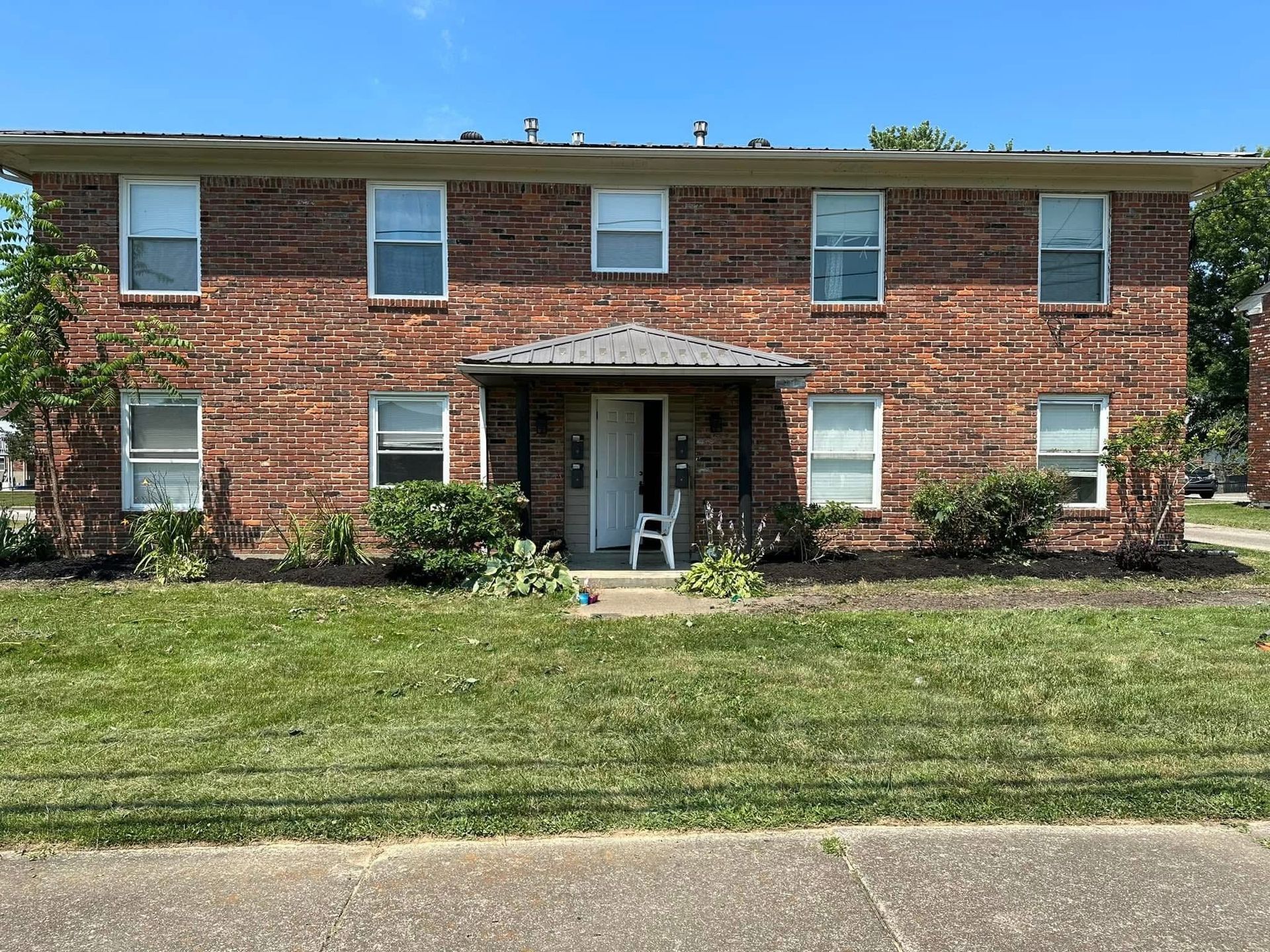 Two-story brick apartment building with white-trimmed windows, central entrance, and a grassy front lawn.