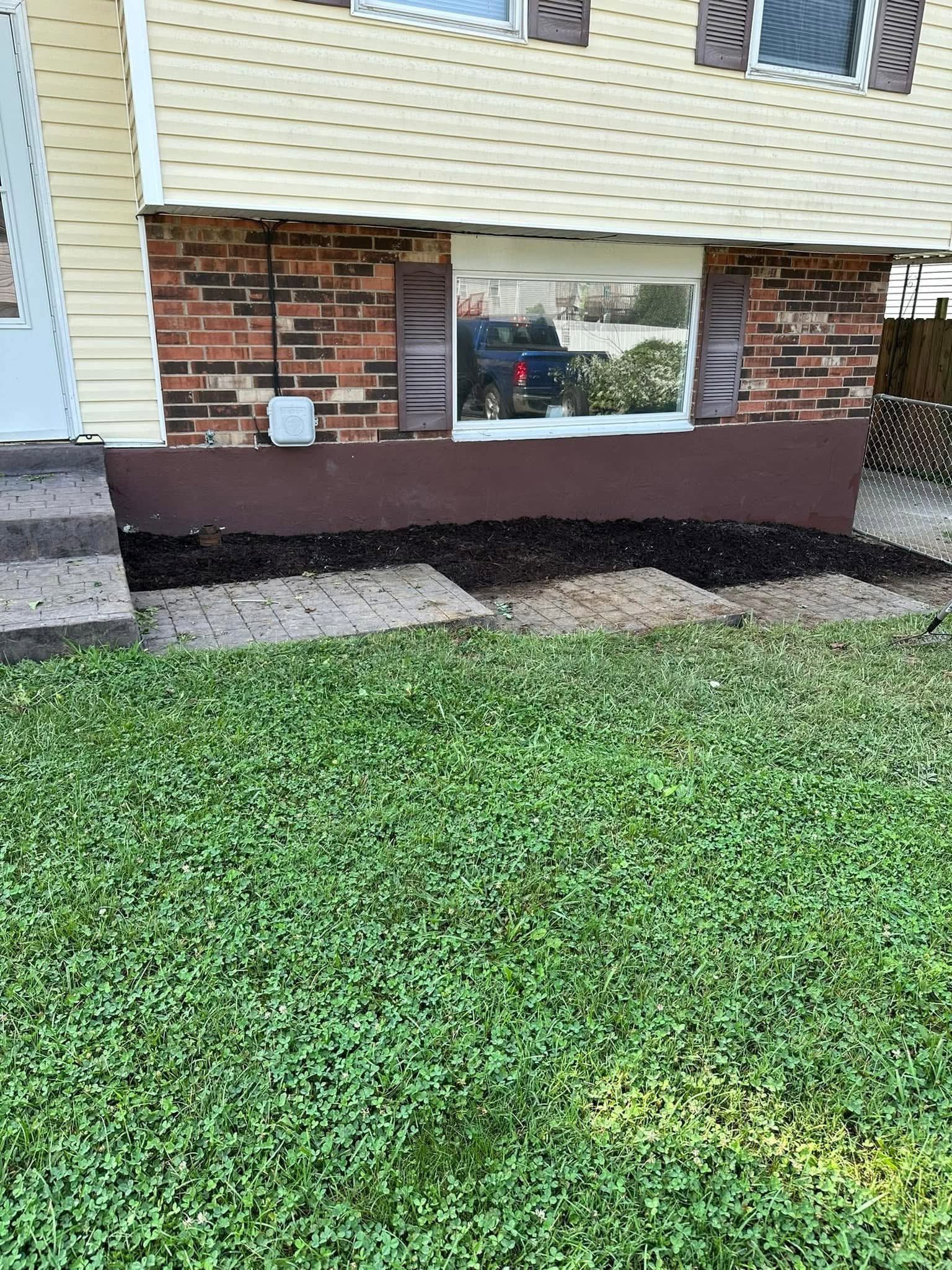 House exterior with brick foundation, white siding, a window, and green grass in front.