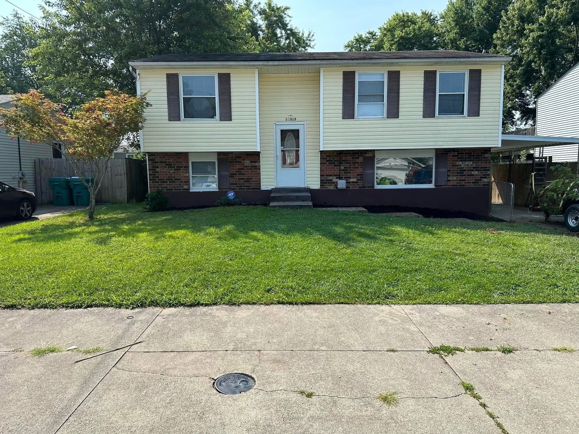 Suburban split-level house with yellow siding, brick base, and a green front lawn under a clear sky