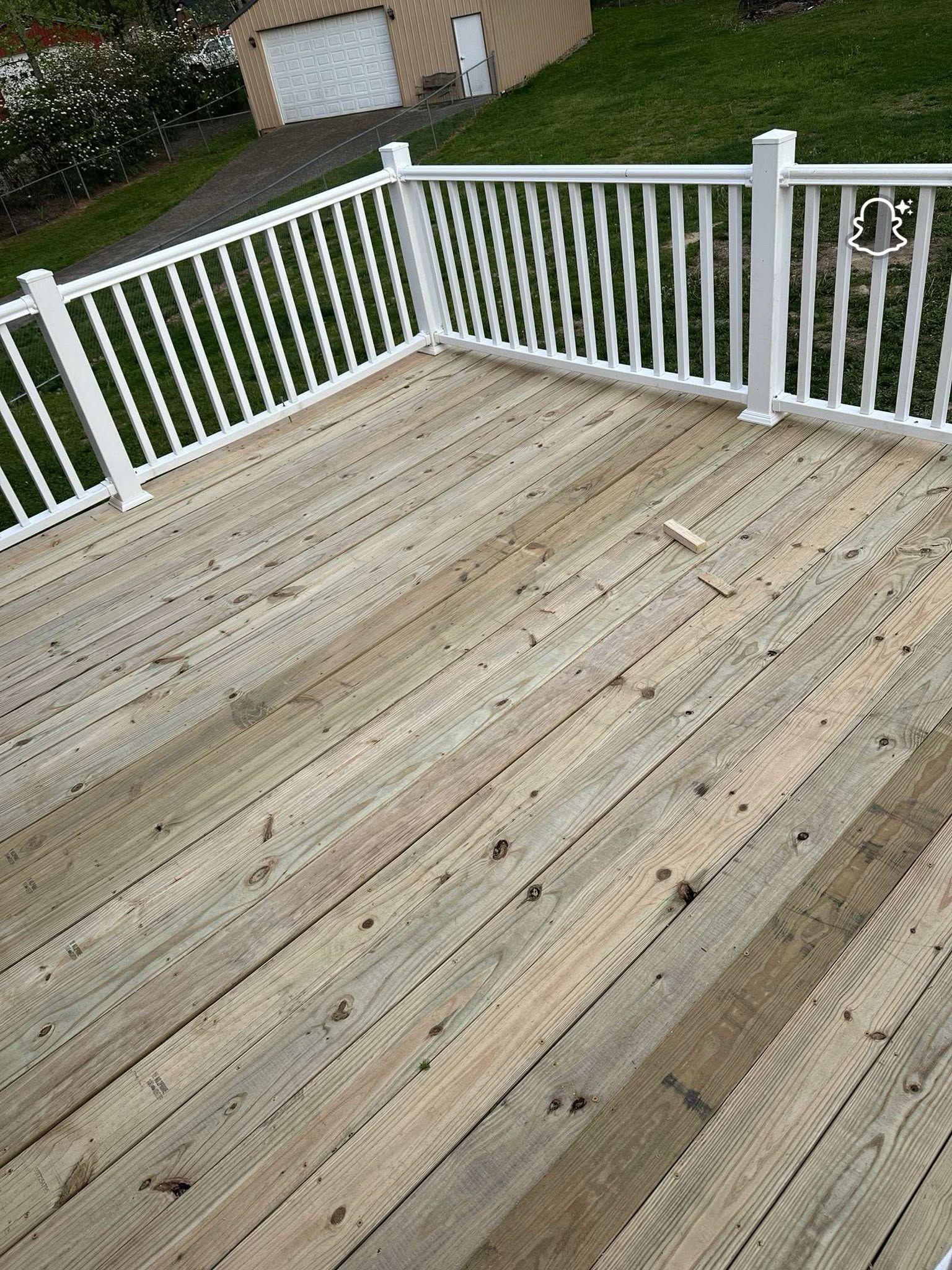 Weathered wooden deck with white railings overlooking a grassy yard and garage.