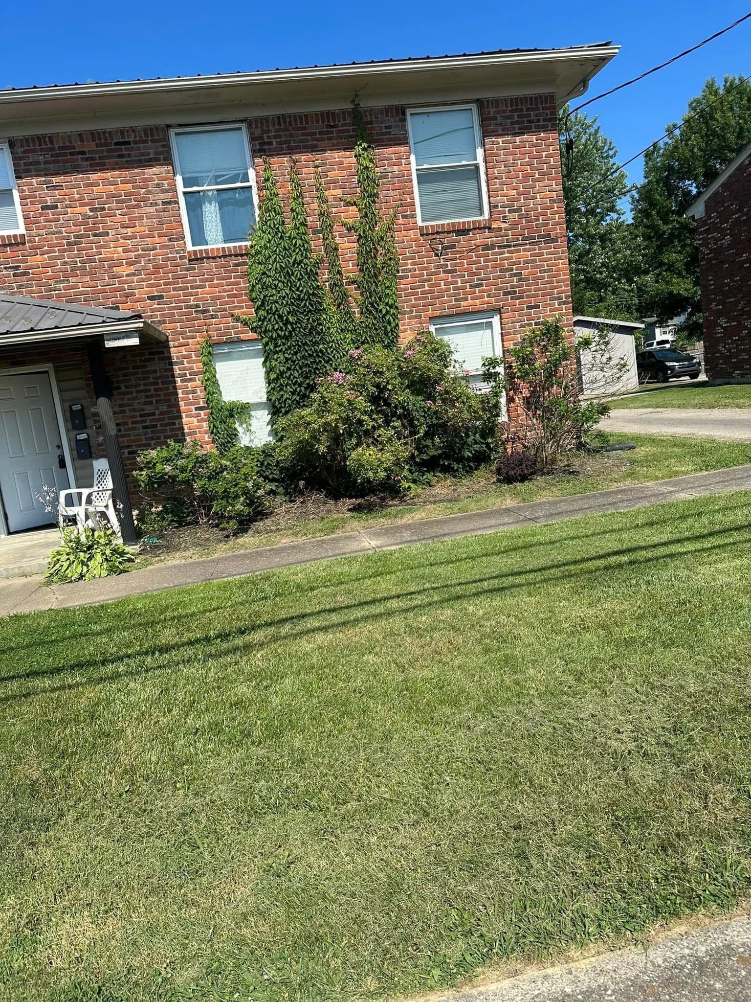Two-story brick townhouse with a green lawn and shrubs under a clear blue sky