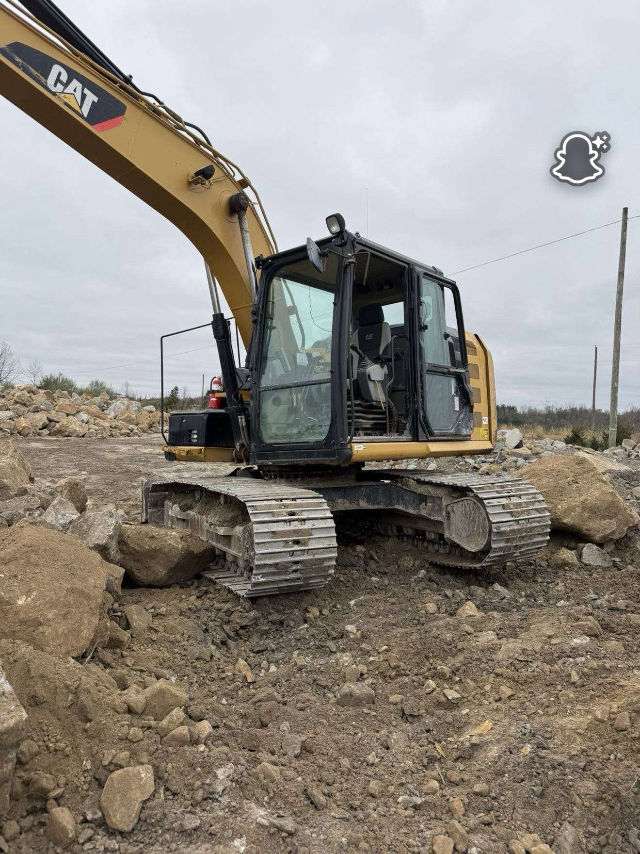 Yellow CAT excavator parked on a rocky construction site under an overcast sky.