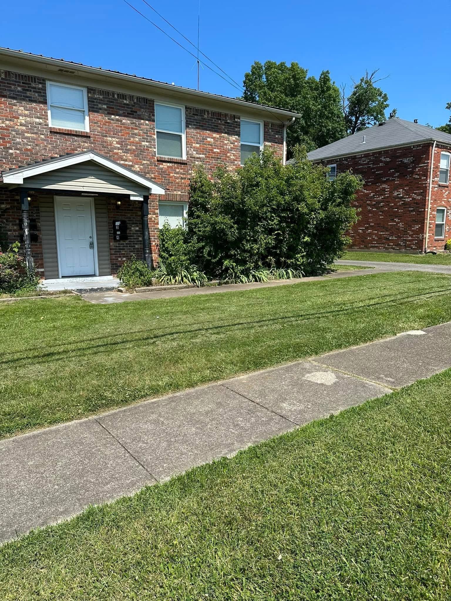 Two-story brick apartment building with a white entrance, lawn, and sidewalk on a sunny day