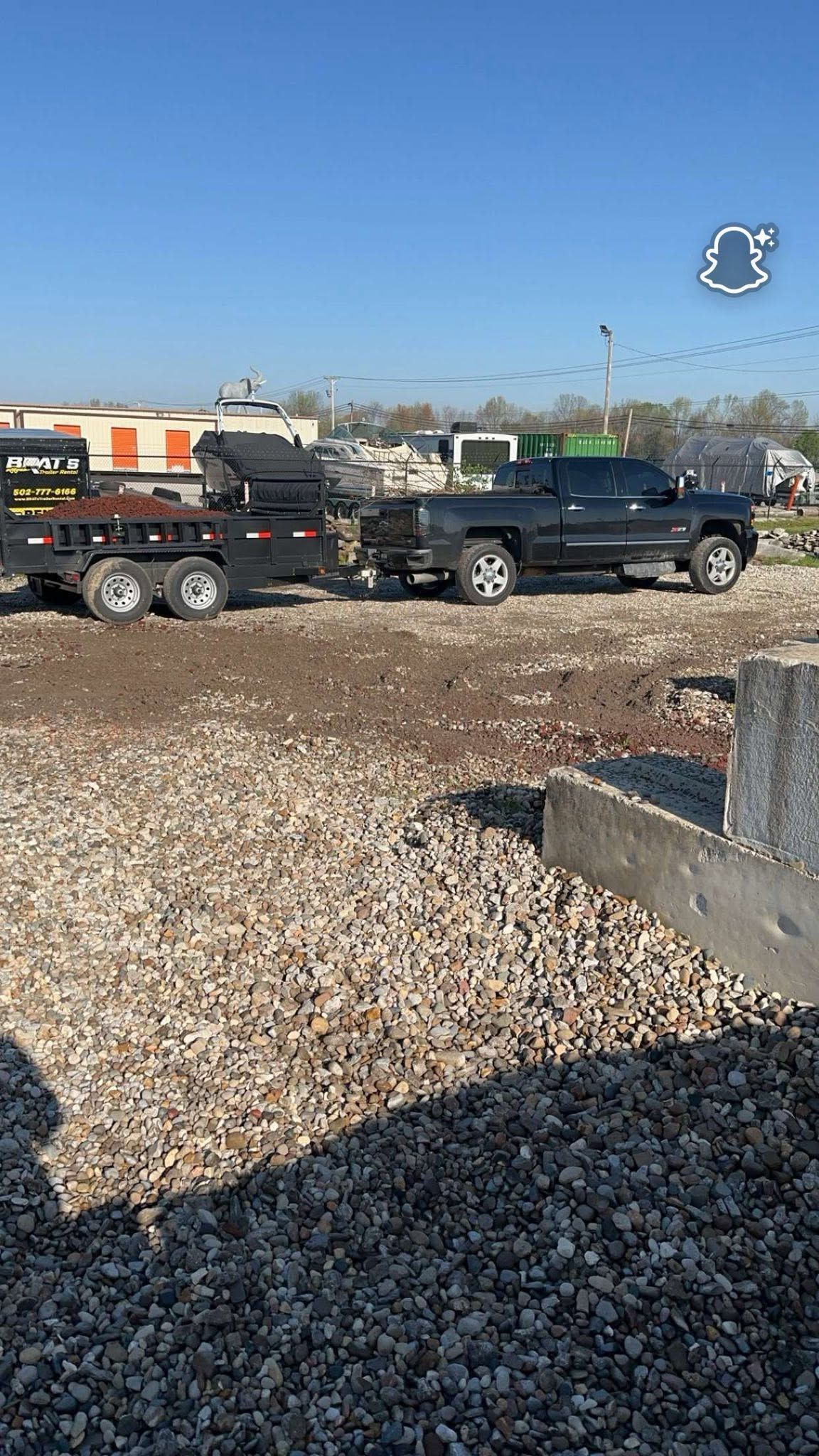 Two black pickup trucks parked on gravel in a sunny lot under a clear blue sky.