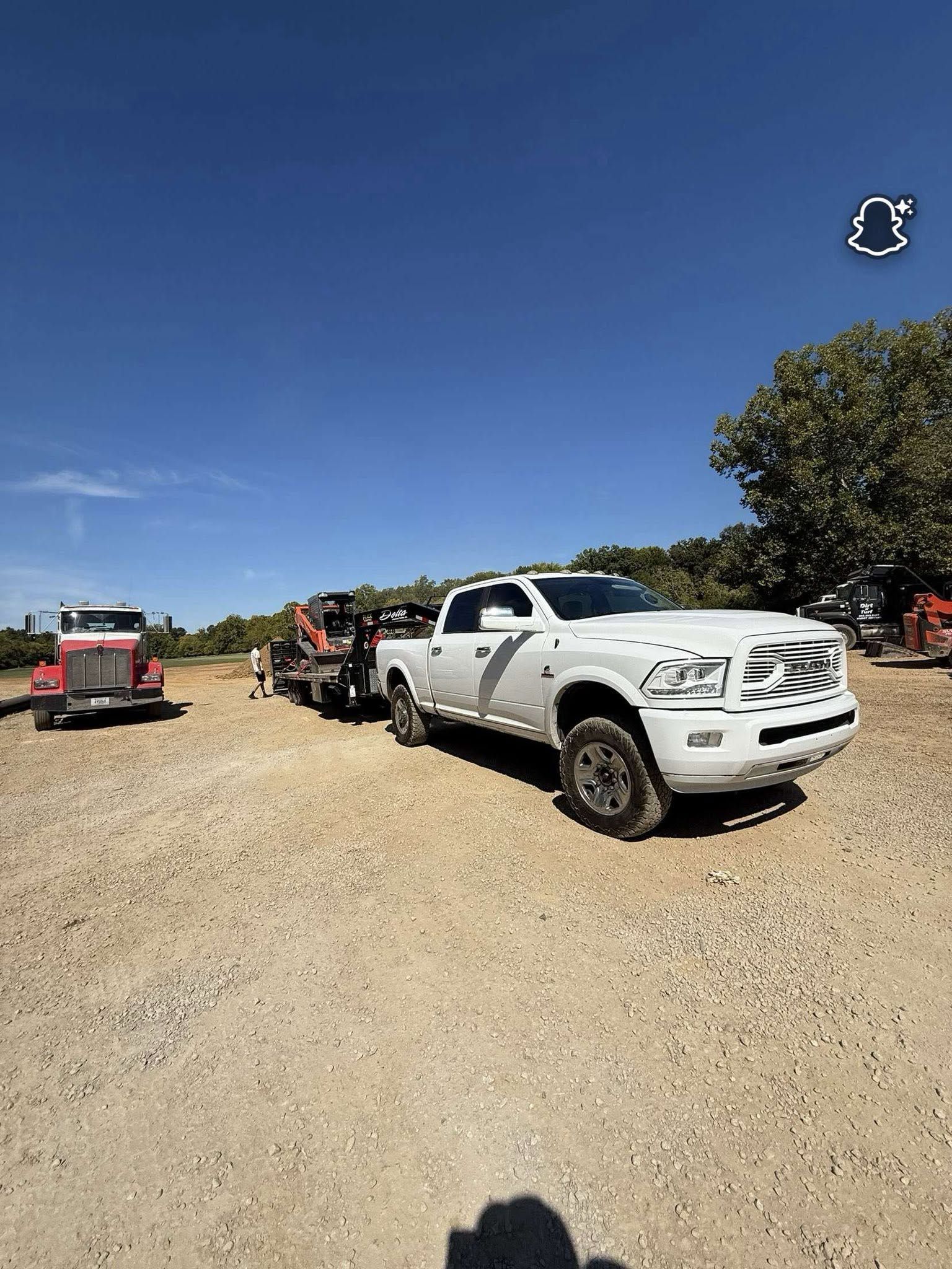 White pickup truck parked on a gravel lot beside red construction equipment under a clear blue sky