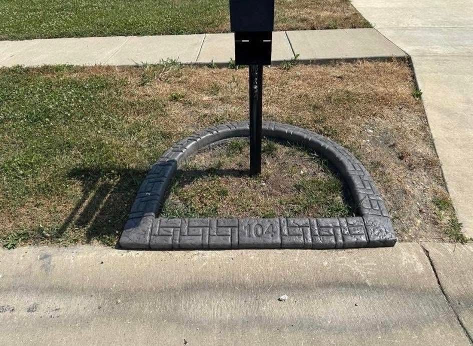 Mailbox in a small brick-bordered patch beside a sidewalk and curb.