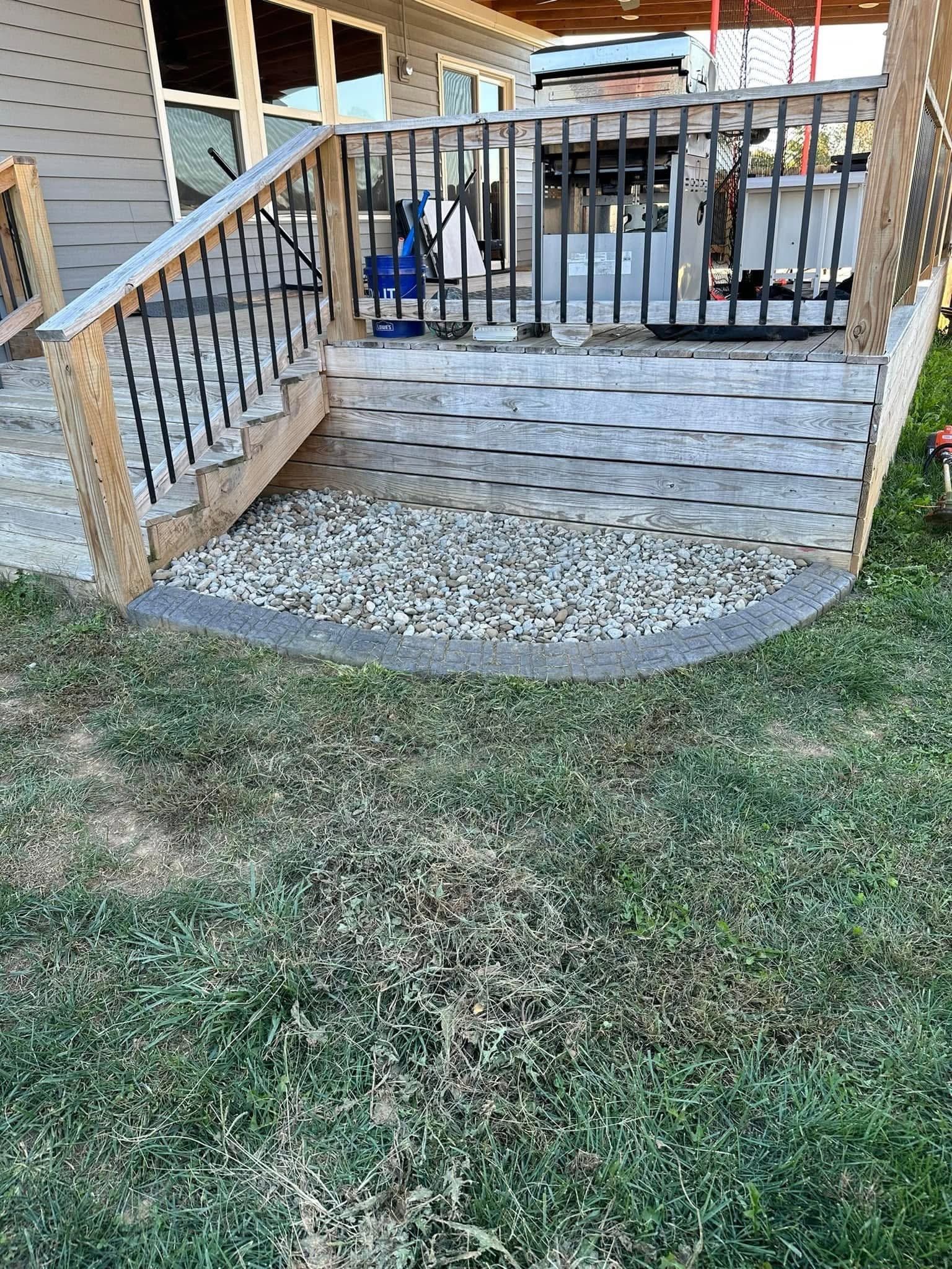 Front porch with wooden steps, black railing, and a gravel landing beside a grassy yard