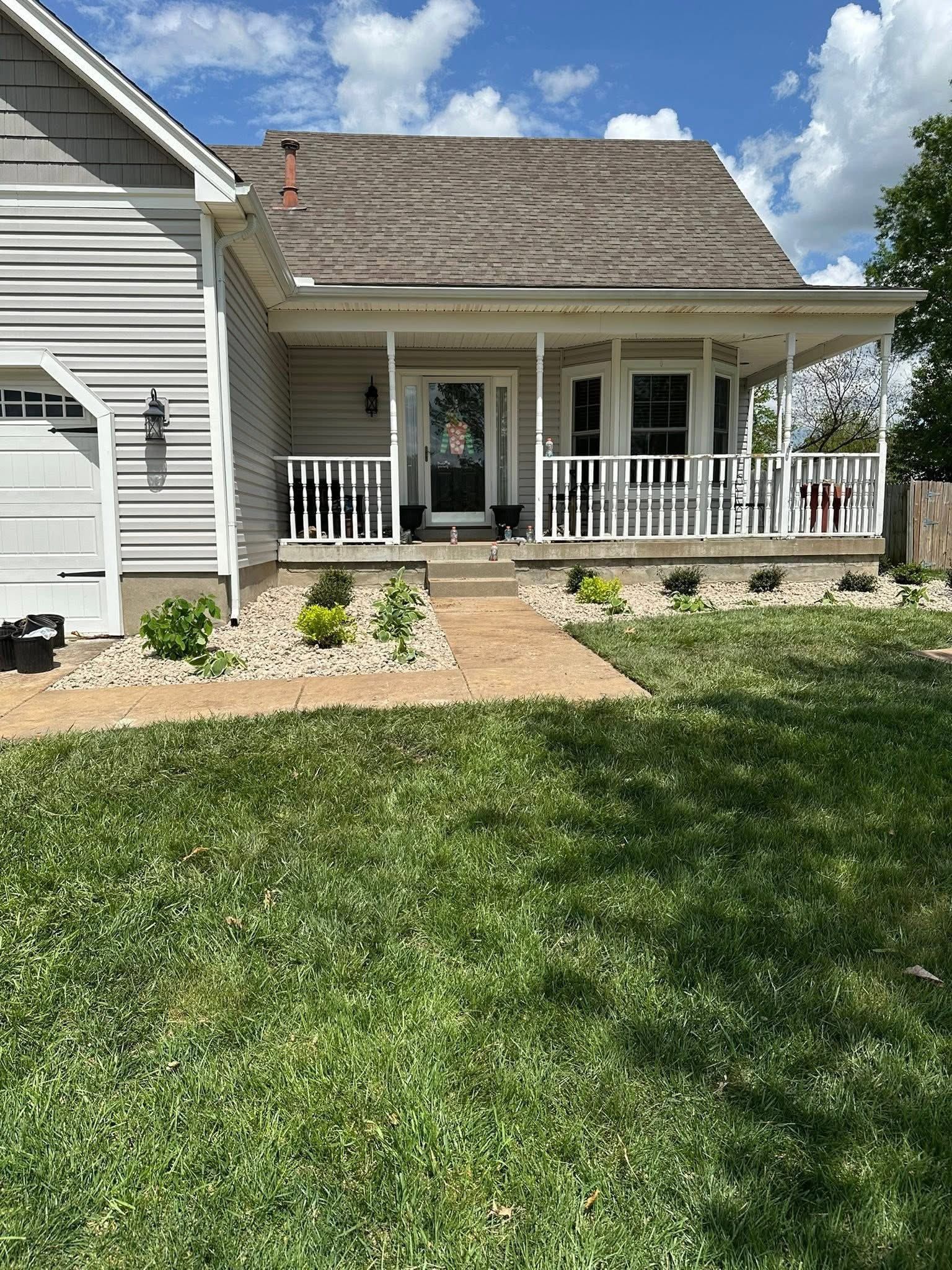 Front porch of a white house with a shingled roof, white railing, and a green lawn under a blue sky.