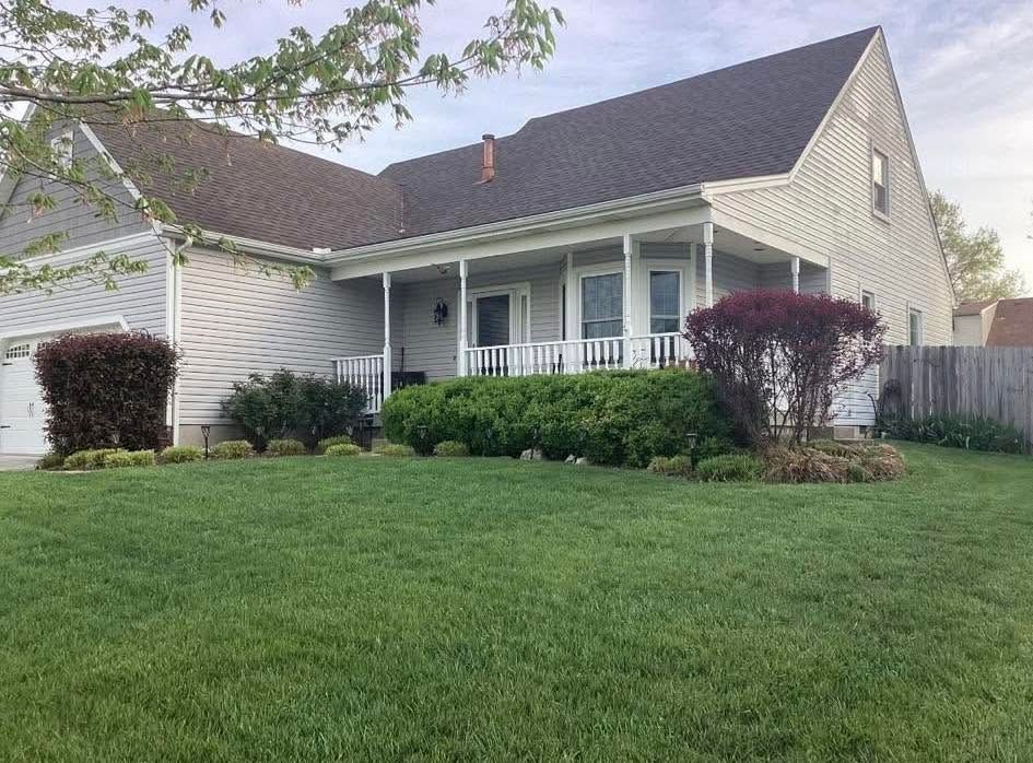 Single-story suburban house with a covered porch, white siding, and a manicured green lawn.