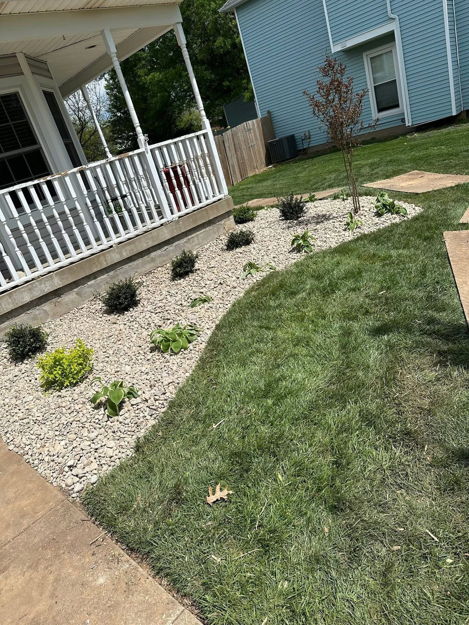 Front porch with white railings beside a gravel bed and green lawn, outside a light blue house.