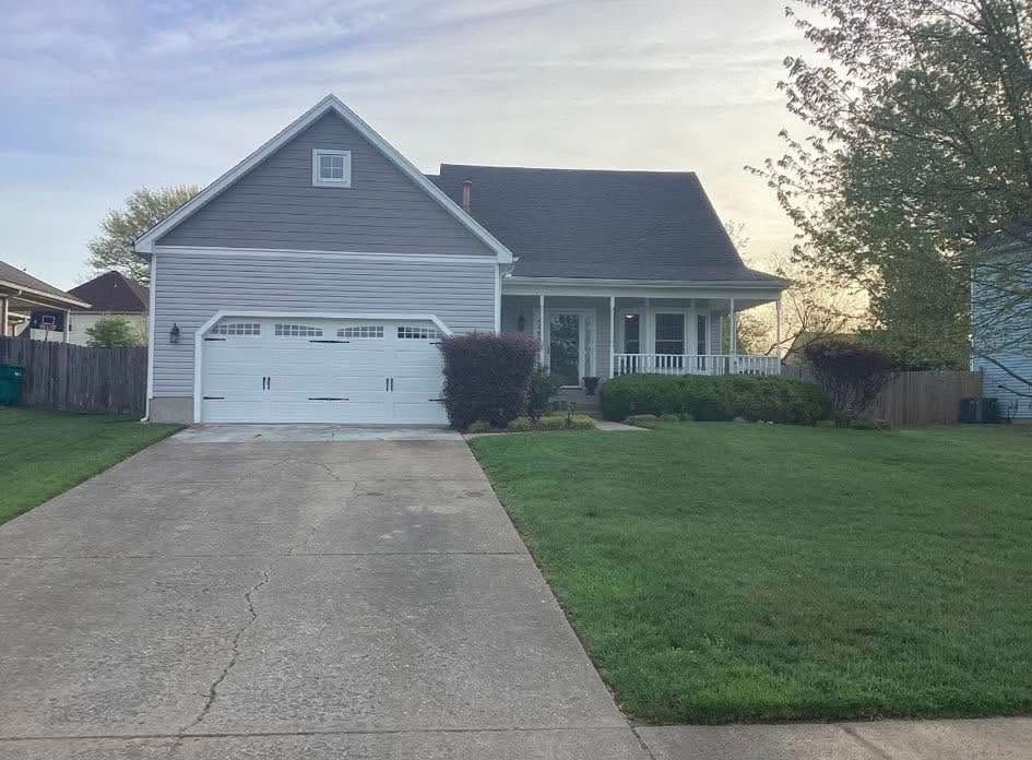 Suburban gray house with a white garage, front porch, and driveway at dusk