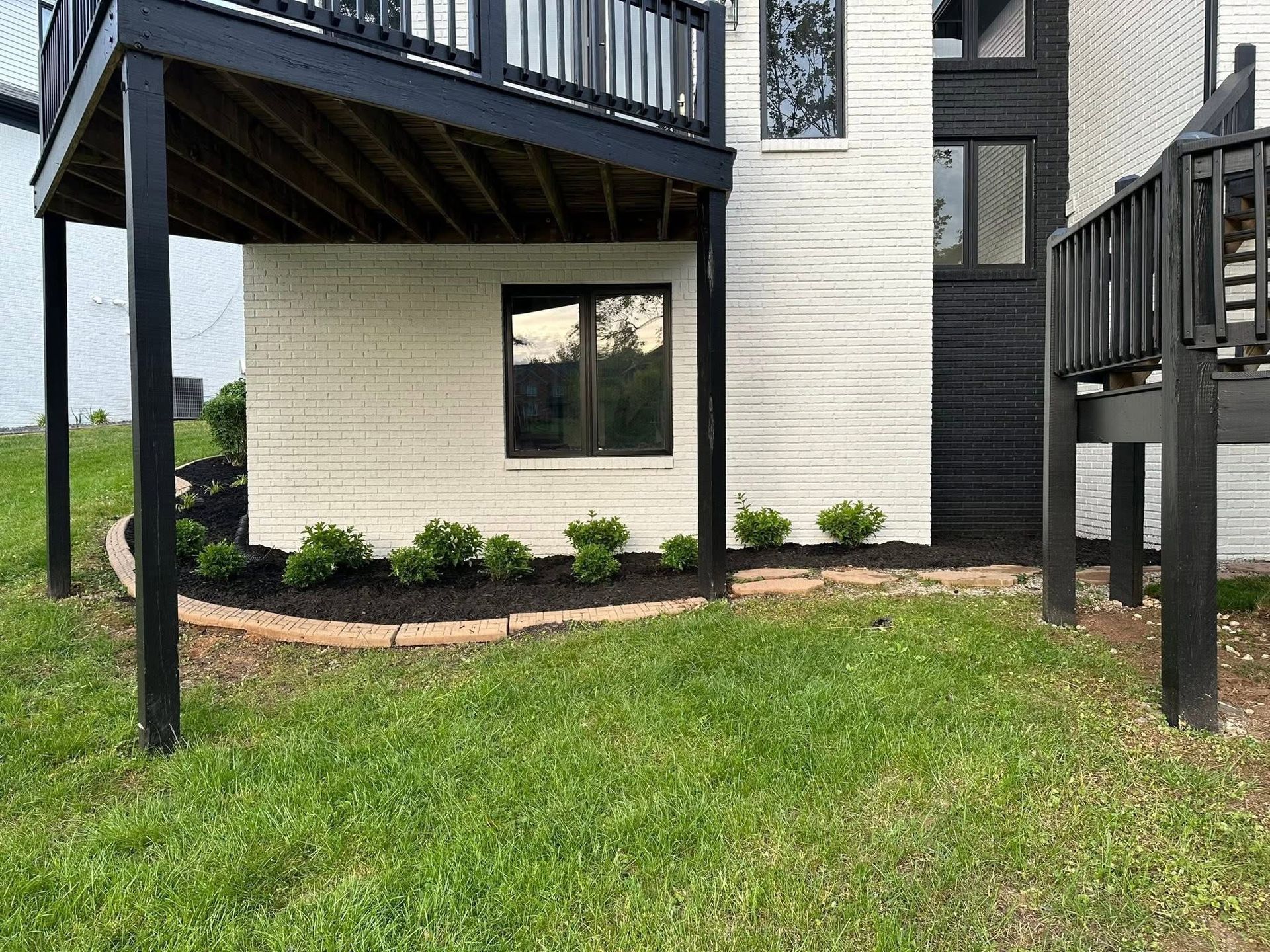 Apartment building exterior with black balconies, beige siding, and small landscaped shrubs by a grassy lawn
