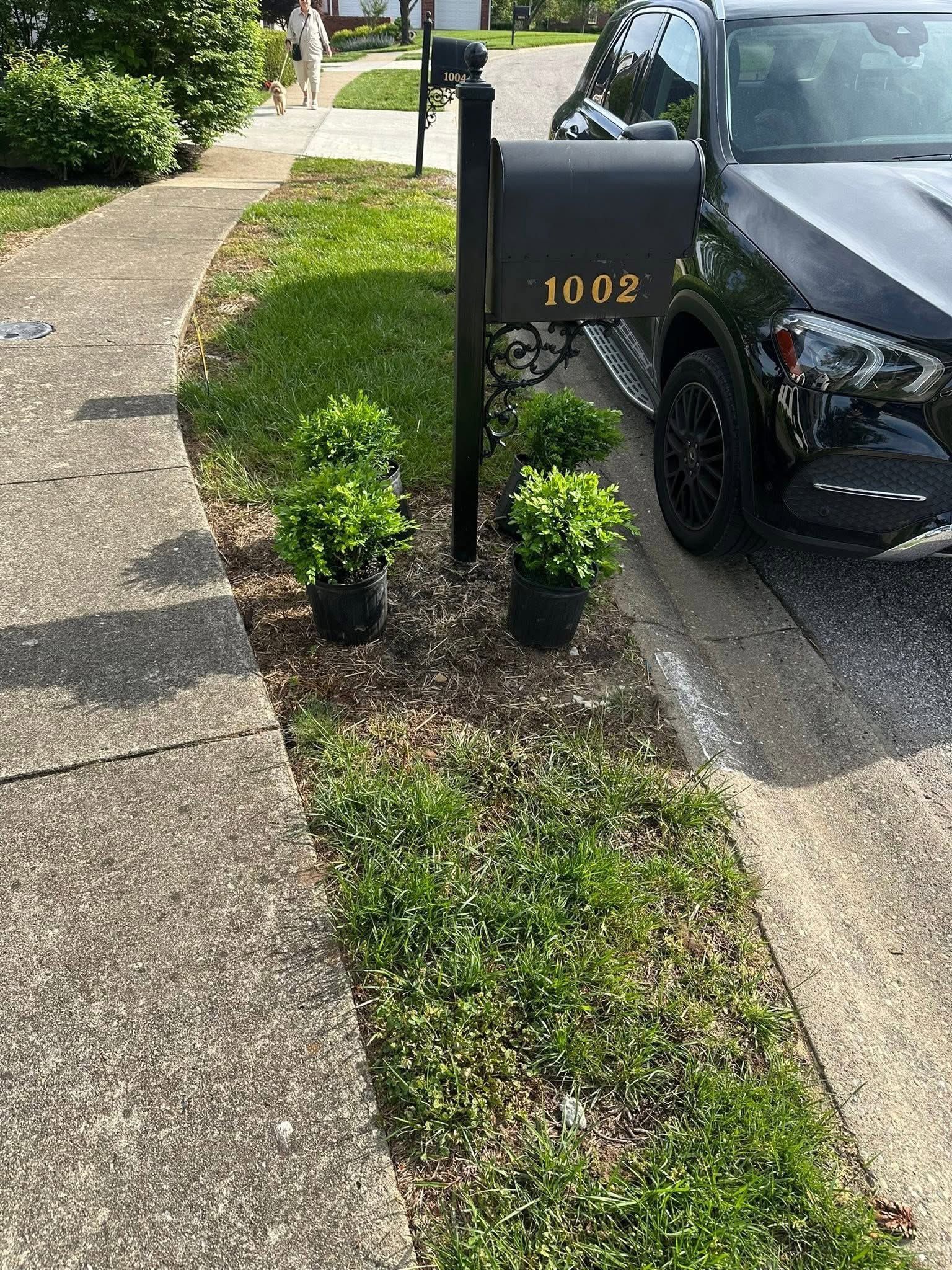 Black mailbox marked 1102 beside a parked black car along a curved sidewalk and driveway.