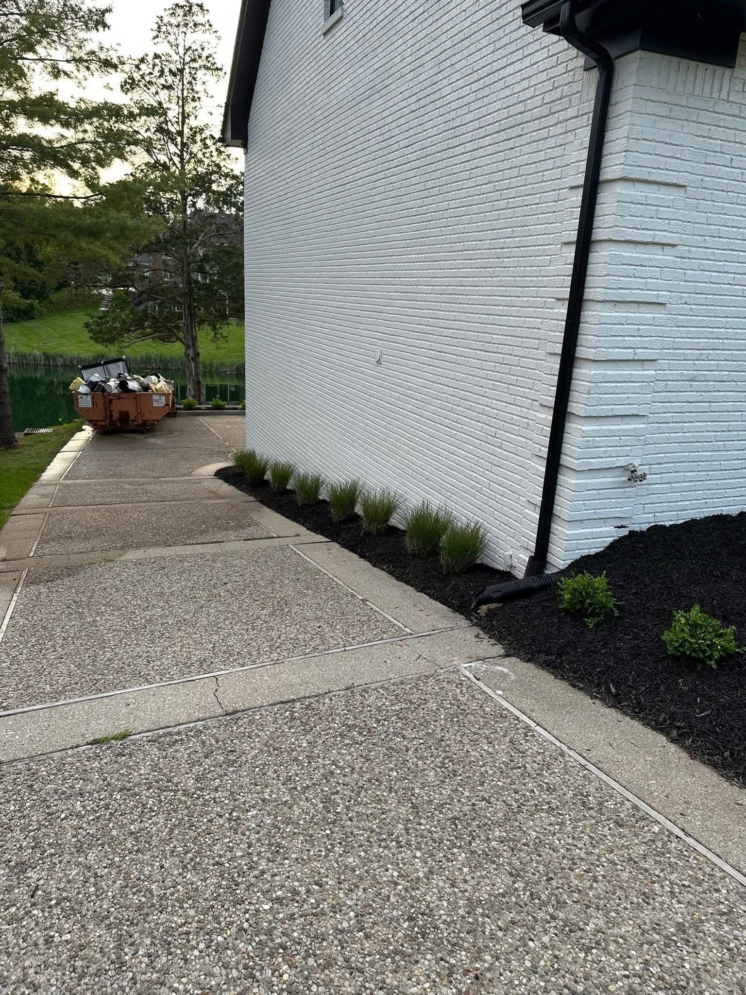 Curved pebble walkway beside a white textured building with potted flowers and greenery