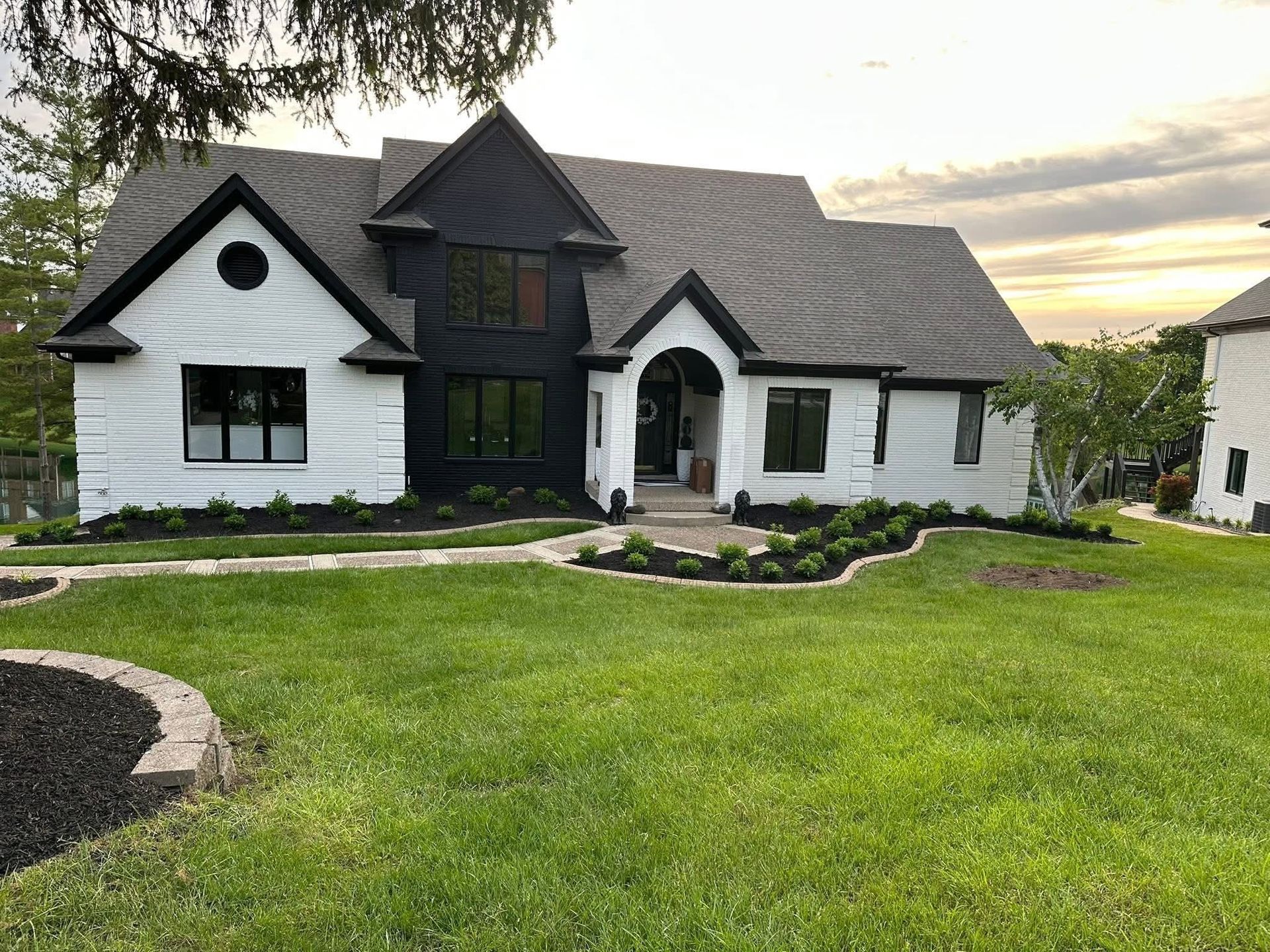 Large two-story white and black house with a manicured lawn and curved stone walkway at sunset