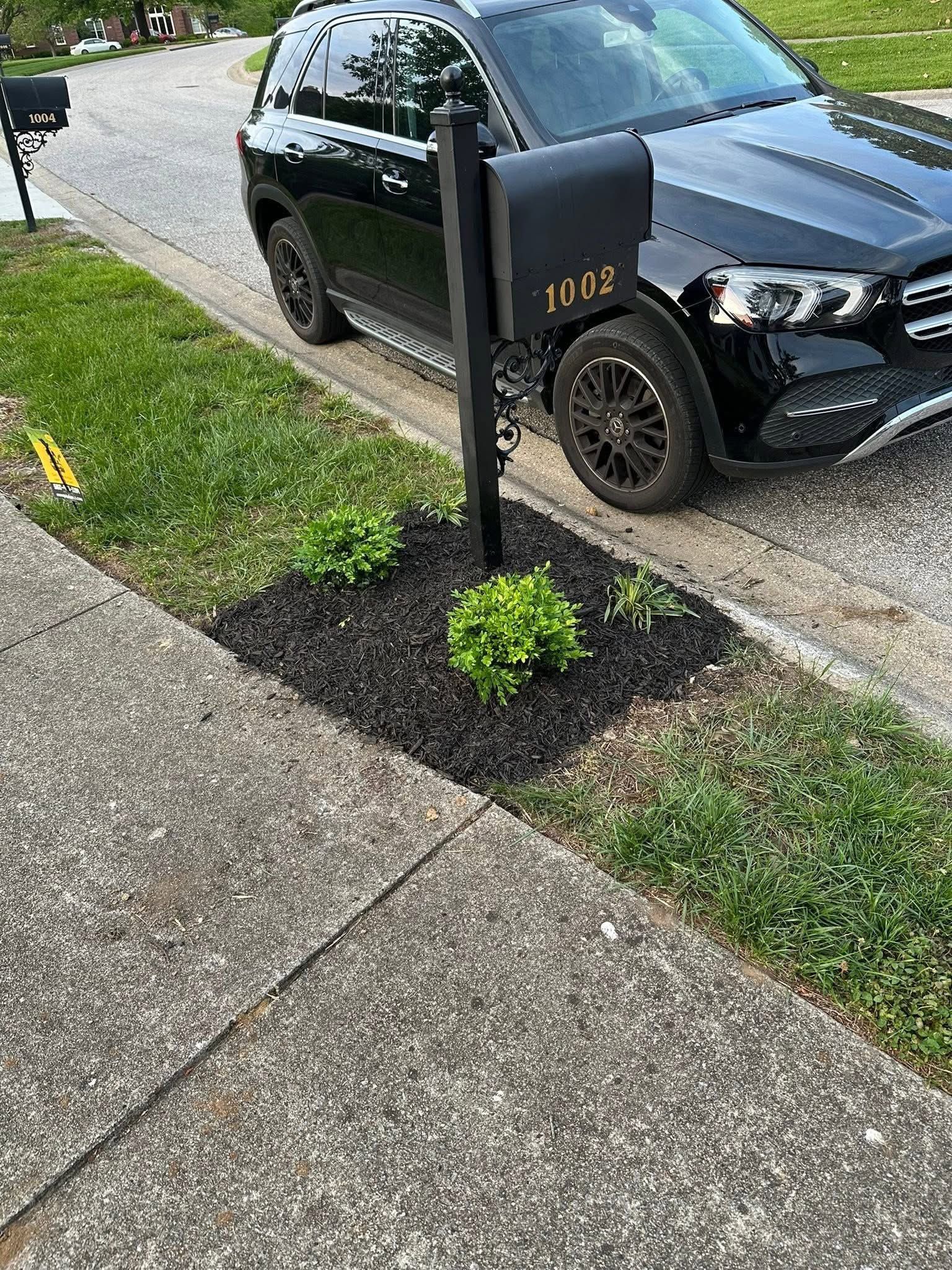 Black SUV parked by a sidewalk beside a black post with gold numbers, next to a small grass patch.