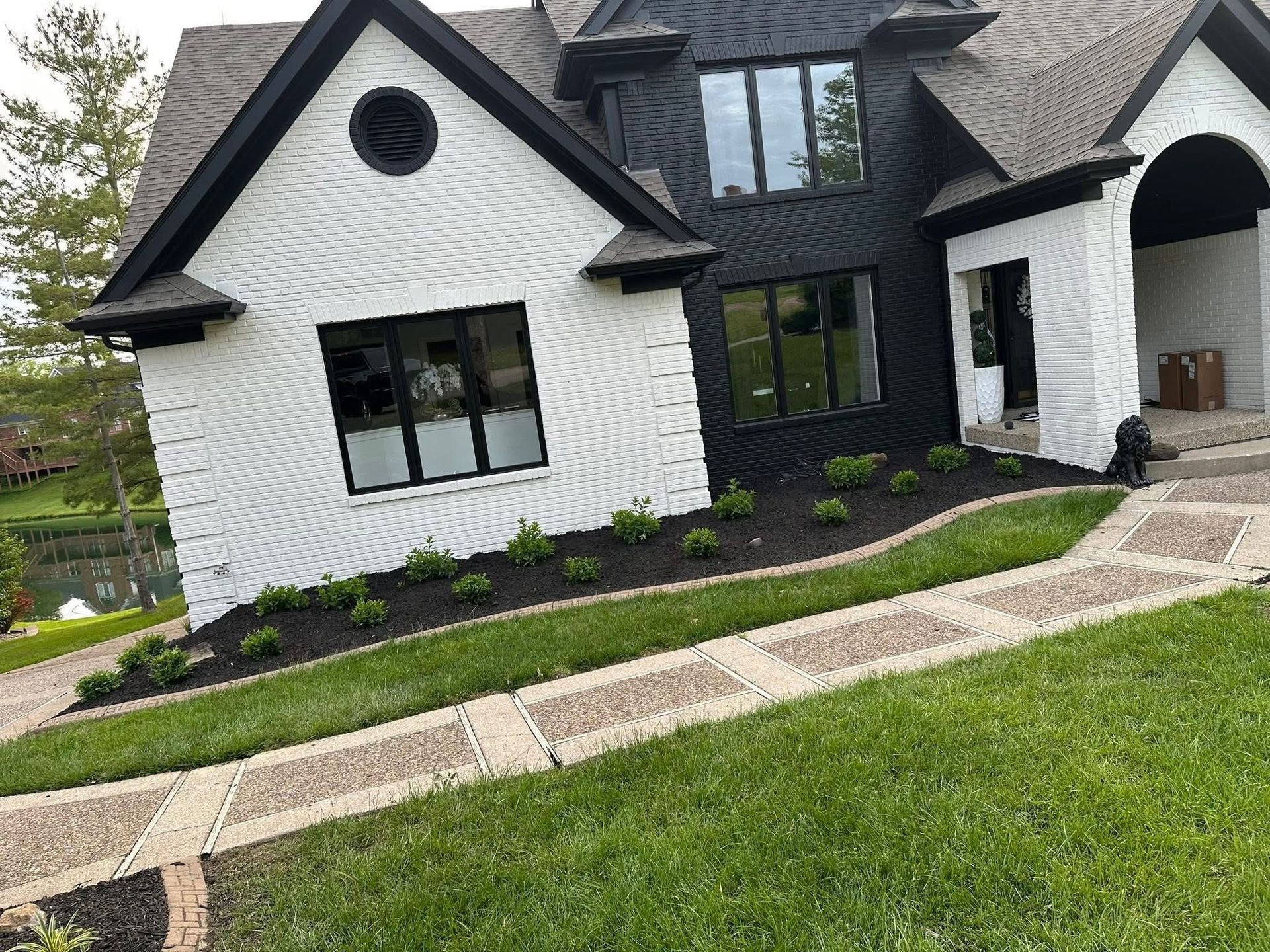 White modern house with black trim, arched entry, front garden, and curved stone walkway