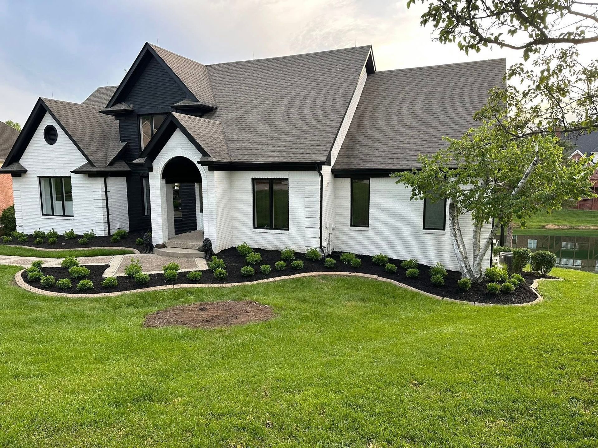 White suburban house with black trim and arched entry, landscaped front yard, and green lawn