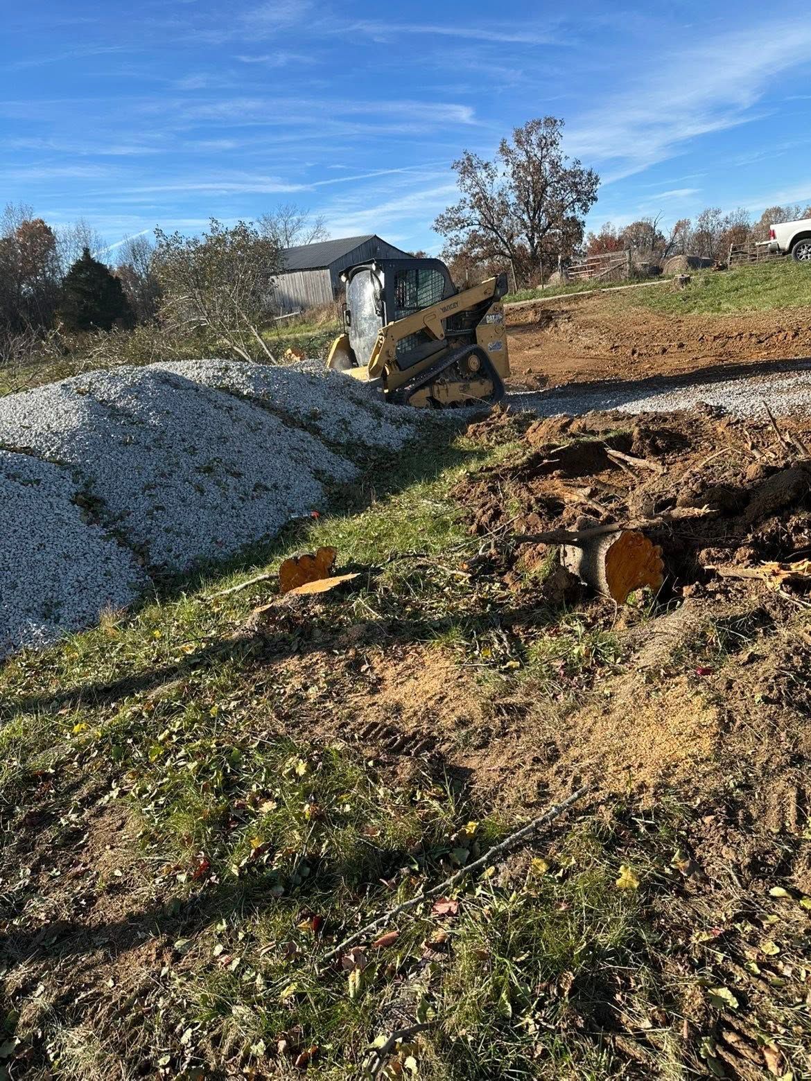 Small excavator on a gravel pile in a grassy field under a clear blue sky