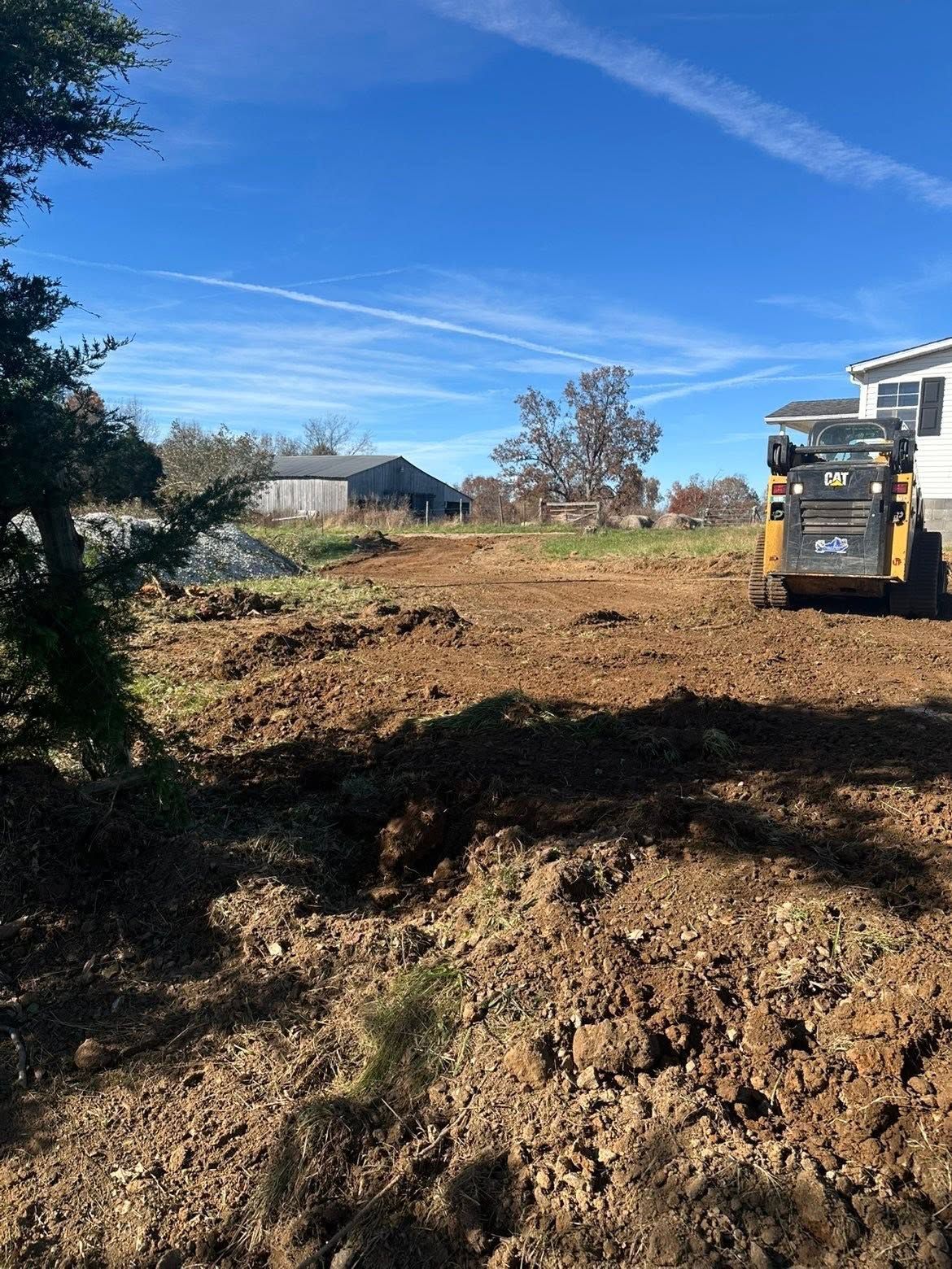 Construction site with excavator clearing dirt in a sunny, open lot under a blue sky.