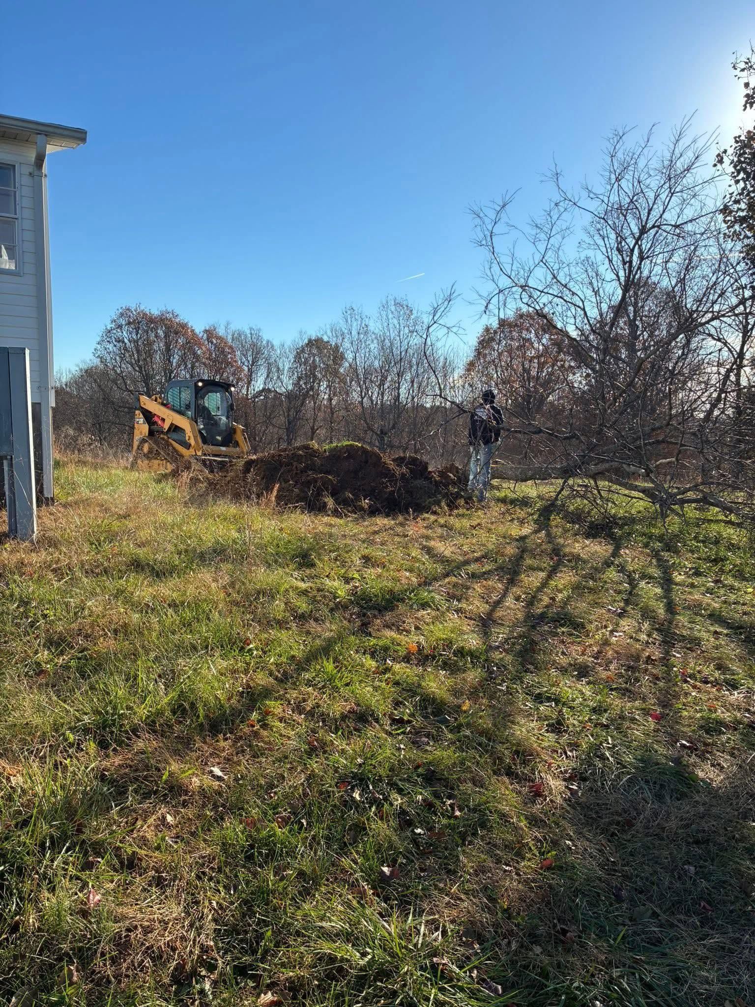 Backyard with grassy slope, bare trees, and an excavator under a blue sky