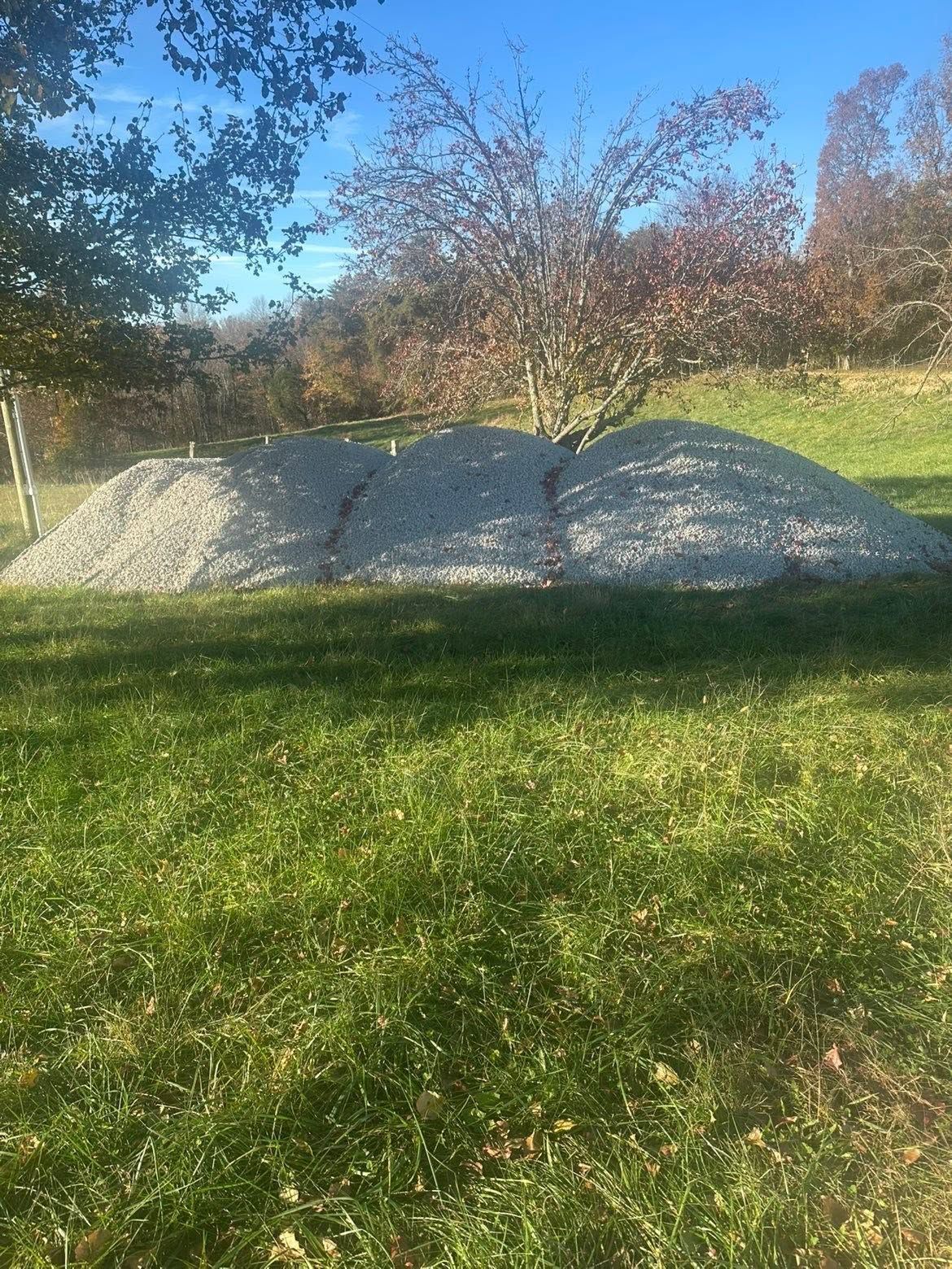 Three white gravel mounds on a grassy lawn under a blue sky with trees in the background