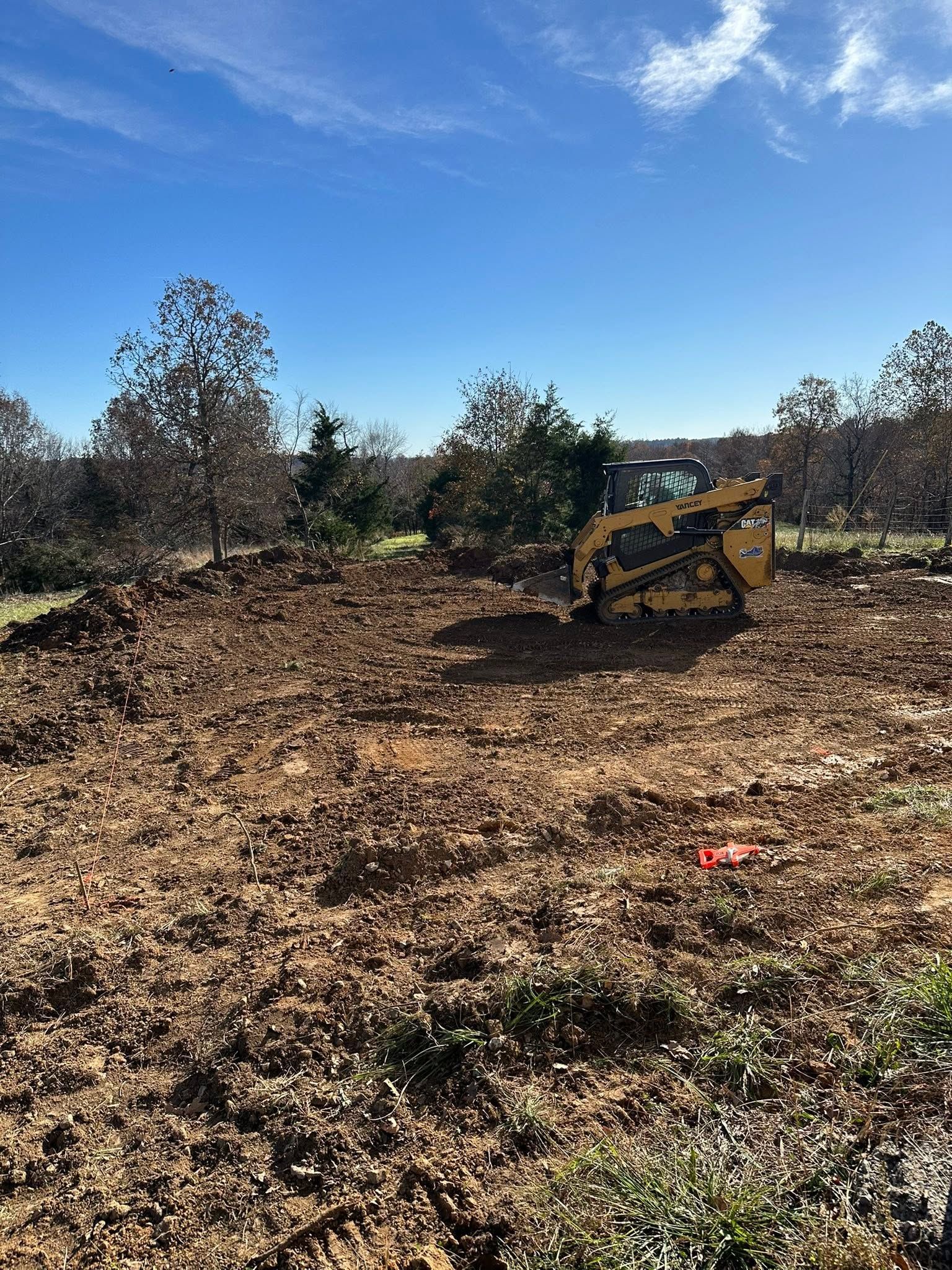 Yellow skid-steer in a cleared dirt field under a bright blue sky with trees in the background