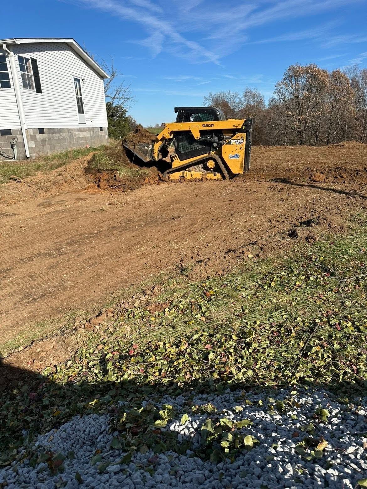 Yellow skid steer digging dirt beside a white house on a sunny lot