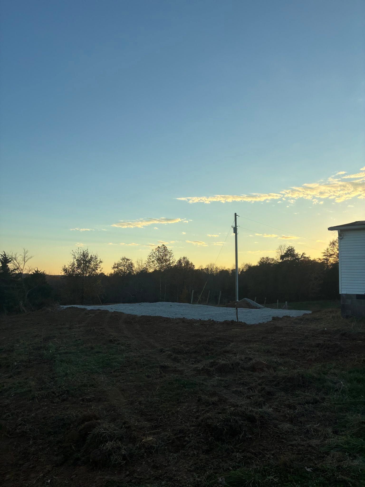 Sunset over a grassy field with a utility pole and a white building edge on the right
