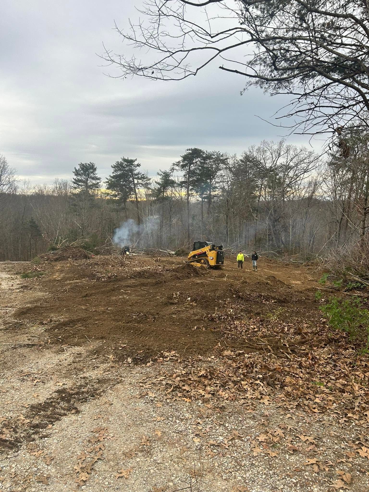 Two workers in yellow gear clearing brush in a smoky wooded area near a gravel path