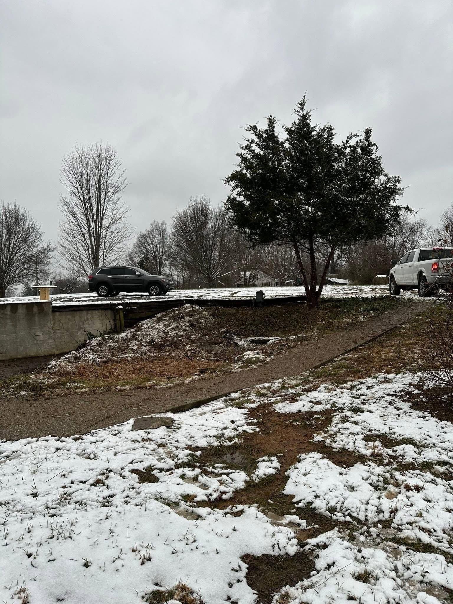 Snowy roadside with trees, a parked car, and a cloudy winter sky