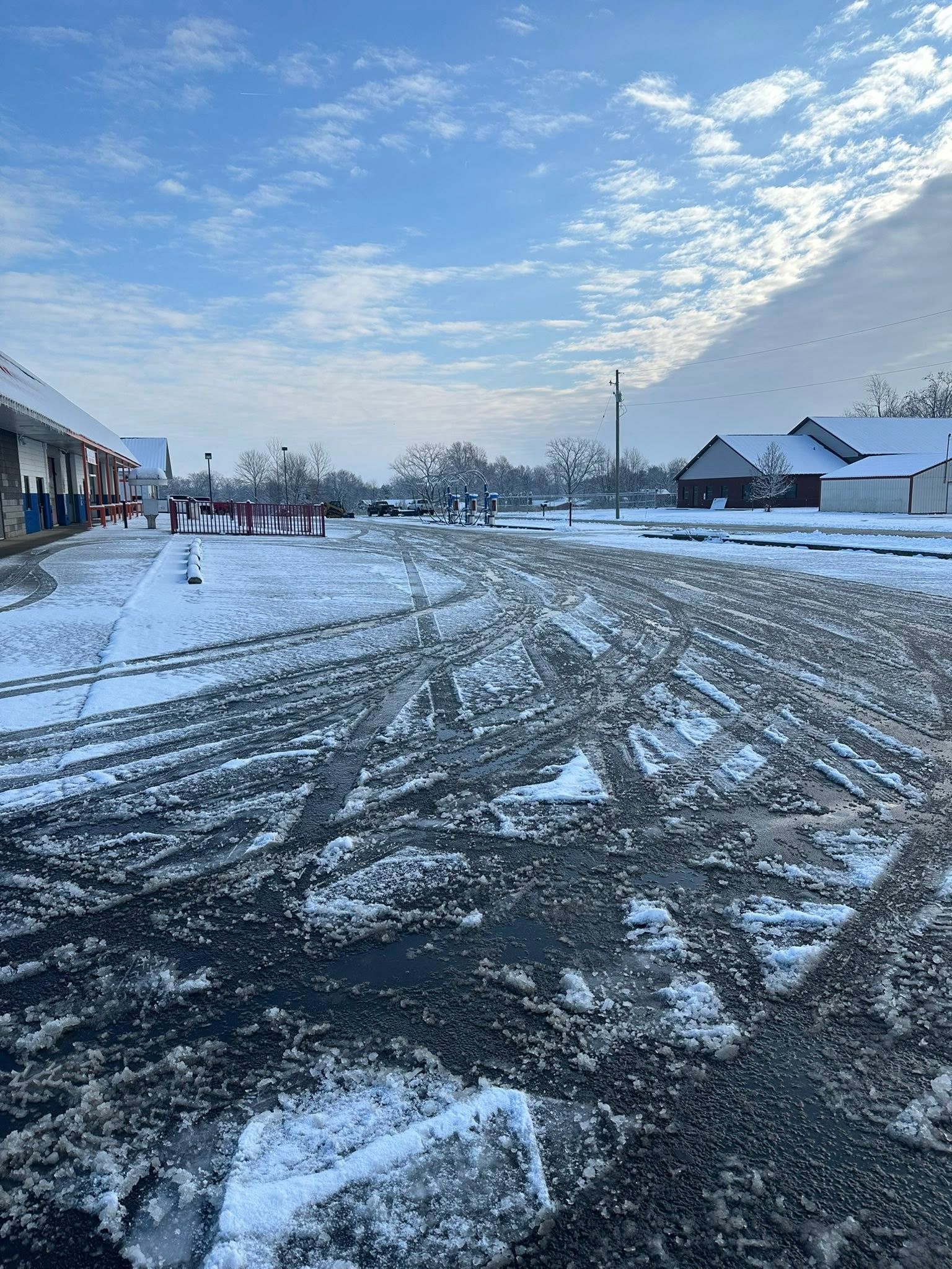 Snowy suburban street with tire tracks, houses, and a cloudy blue sky