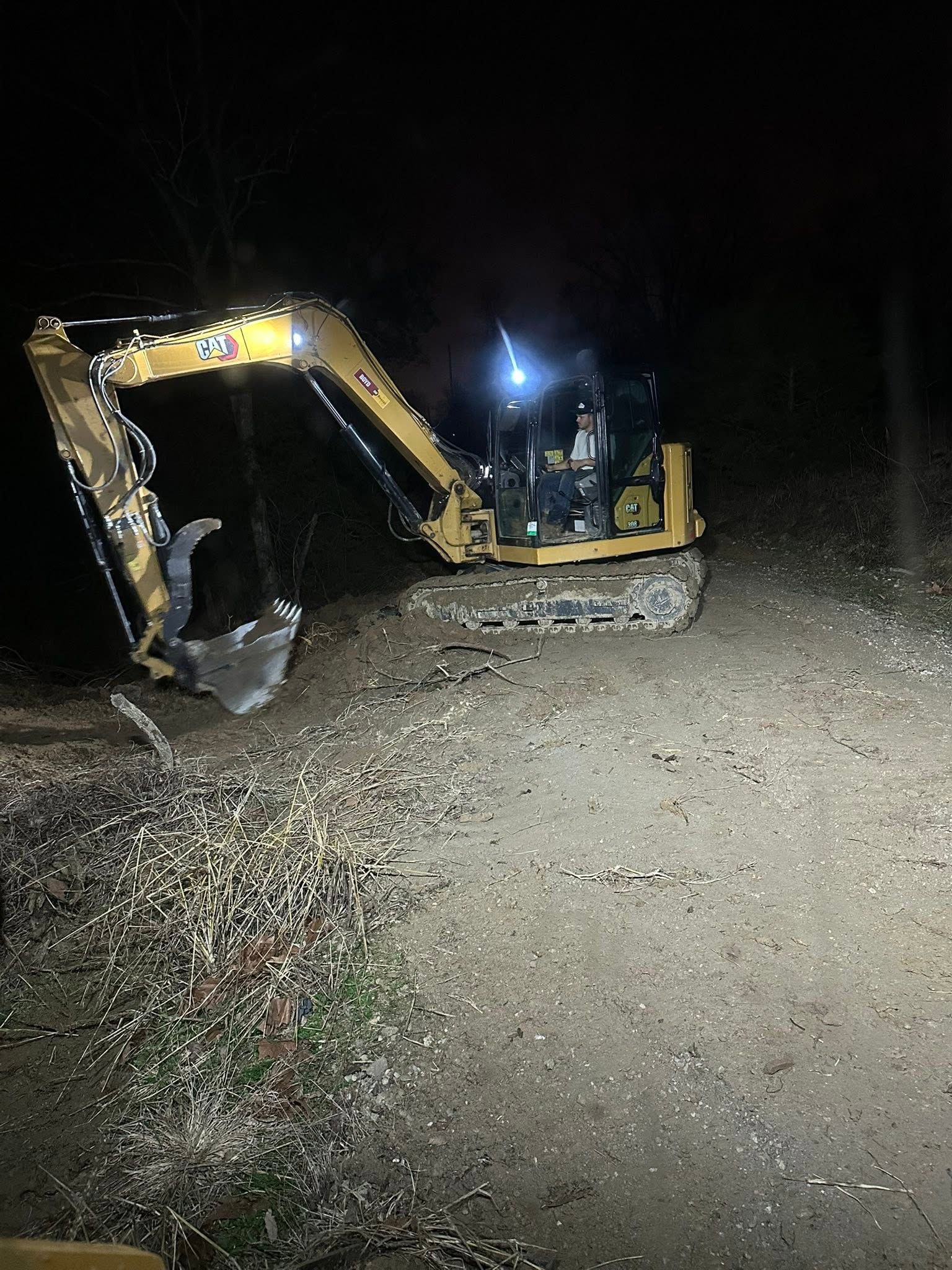 Yellow excavator digging at night on a gravel road, with its lights illuminating the dark surroundings.