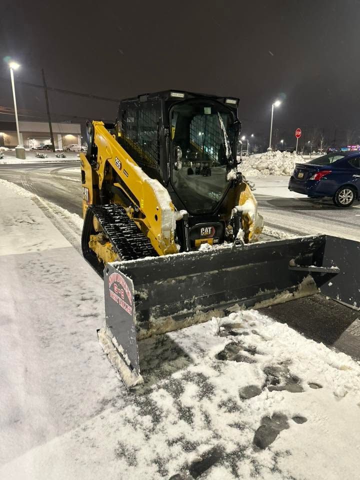 Yellow skid steer with a plow clearing snow in a parking lot at night