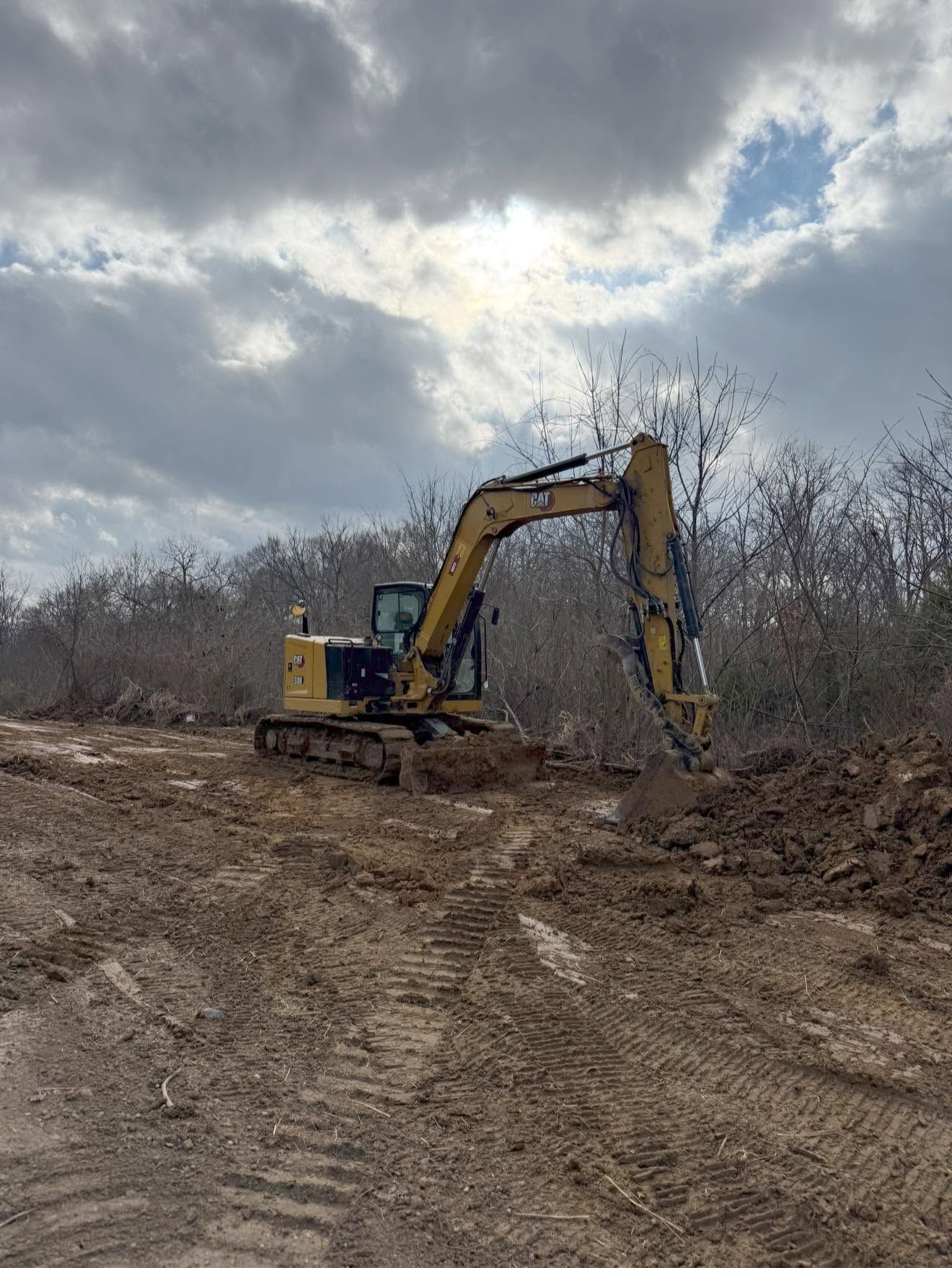 Yellow excavator digging dirt on a muddy site under a cloudy sky
