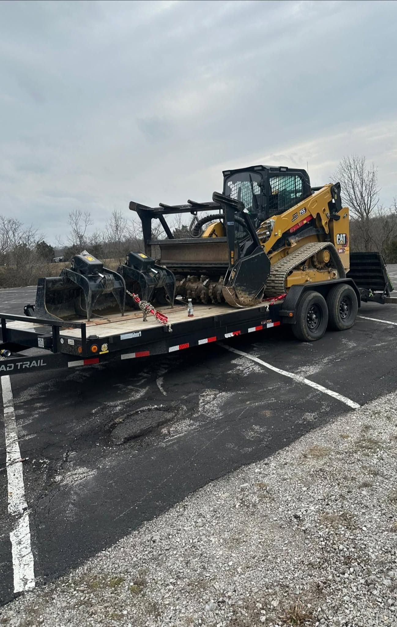 Yellow skid steer loaded on a flatbed trailer in a parking lot on an overcast day