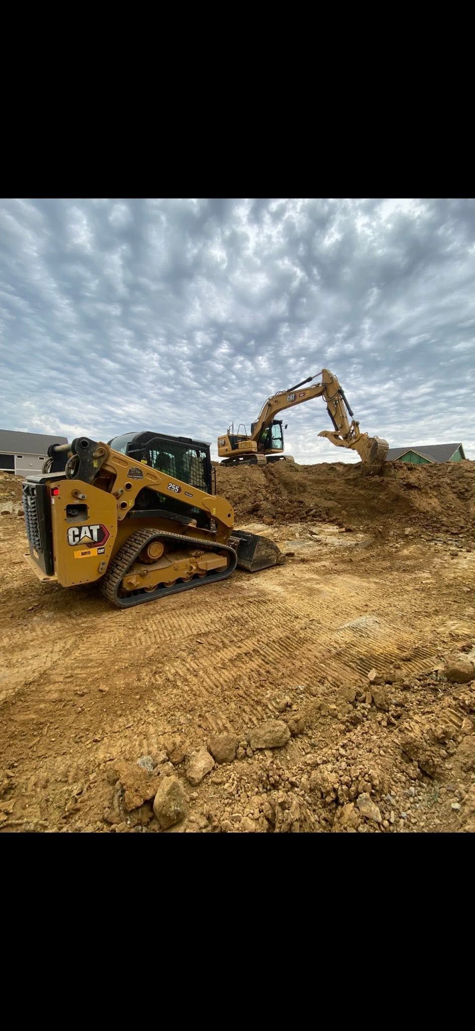 Yellow excavator and dump truck moving dirt at a construction site under a cloudy sky