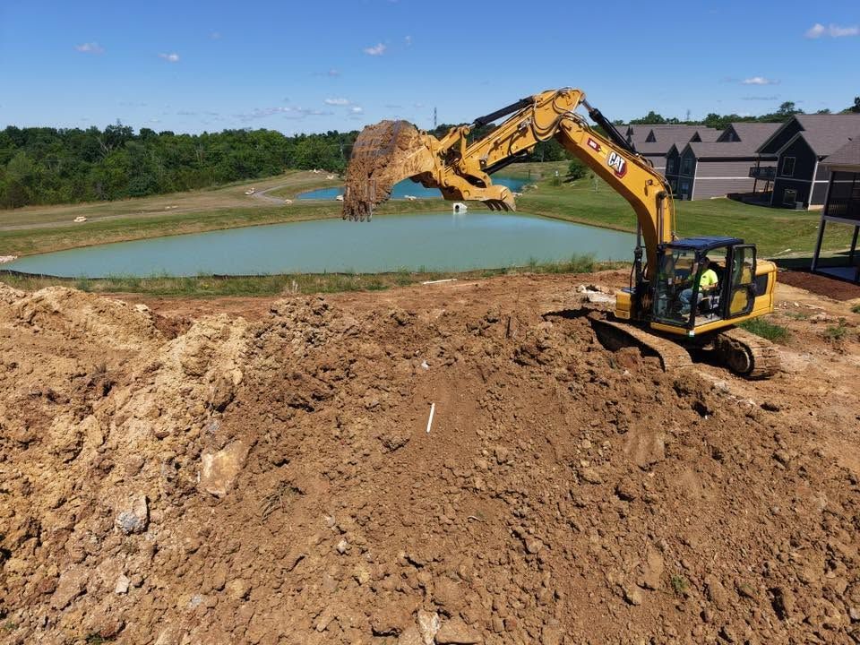 Excavator digging dirt beside a pond at a construction site