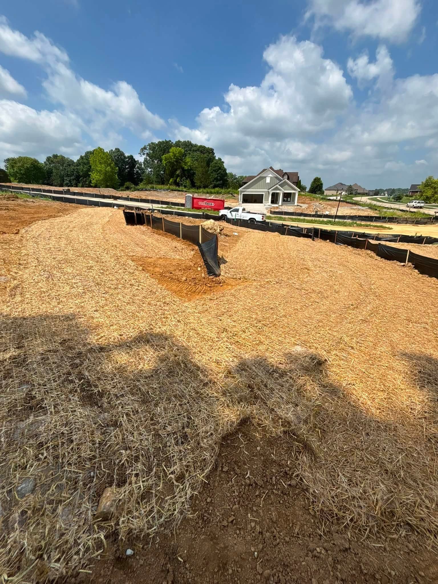 Drying crops spread across a large outdoor yard under a cloudy blue sky, with a small house in the background