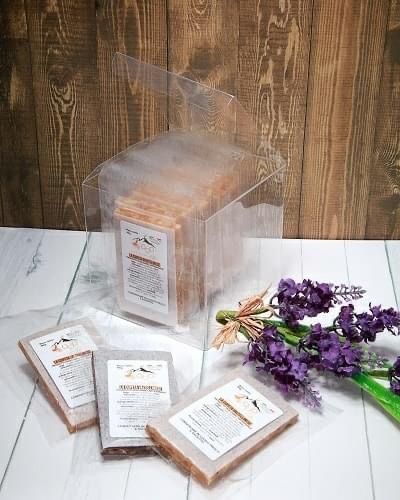 Saponi confezionati in scatole trasparenti e involucri individuali, accanto a rametti di lavanda.