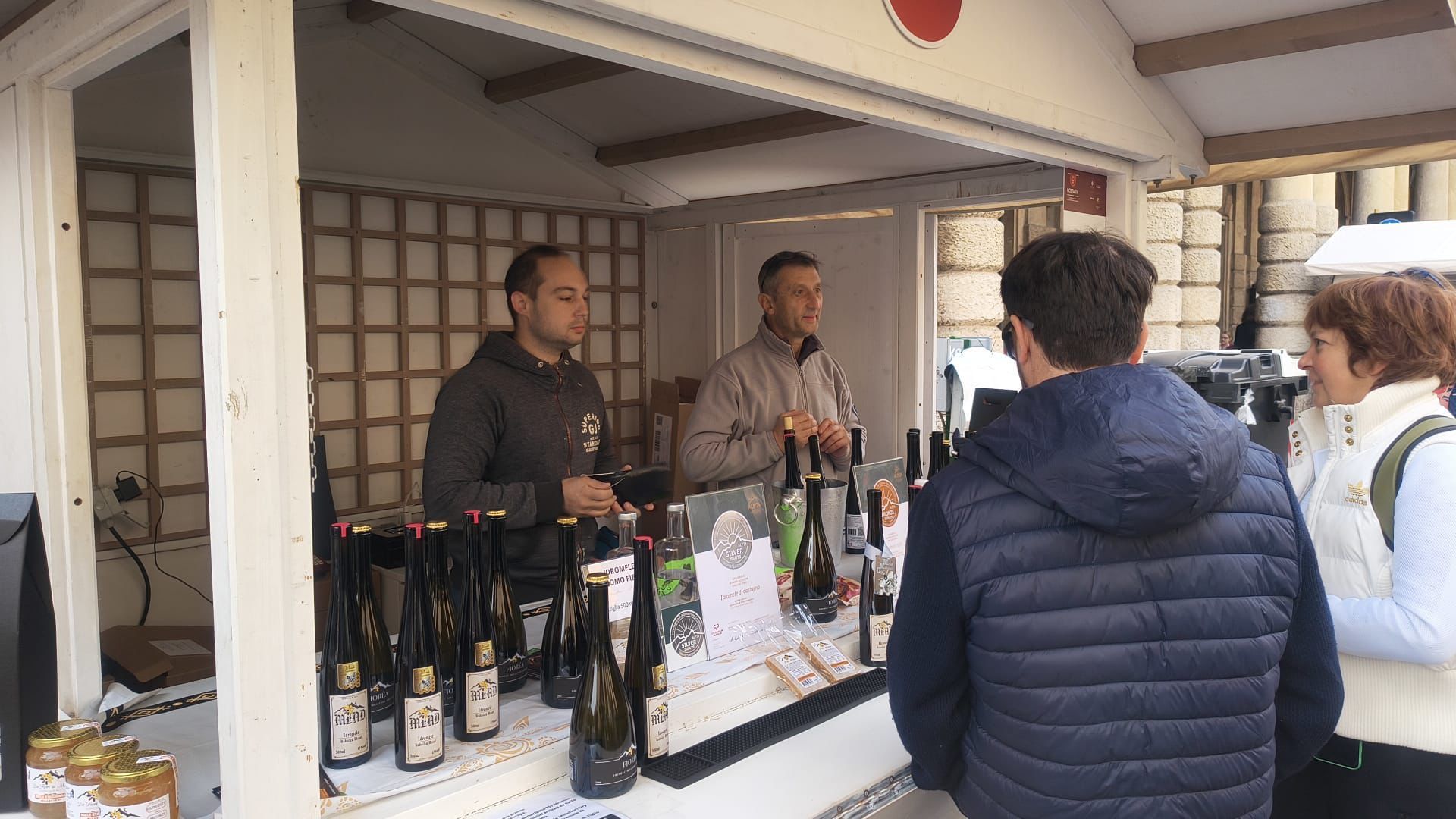 Tre bottiglie di vino con fascette colorate e medaglie a forma di ape su un tavolo.