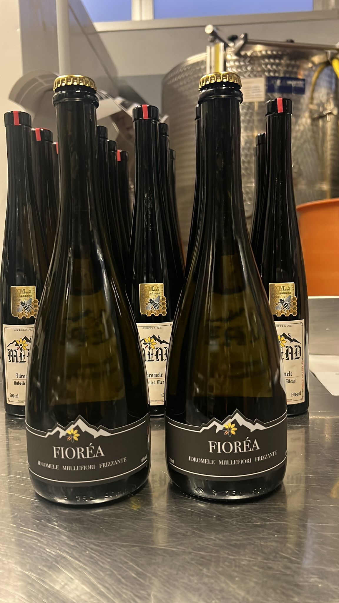 Tre bottiglie di vino con fascette colorate e medaglie a forma di ape su un tavolo.