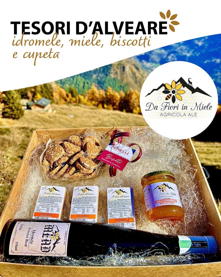 Confezione regalo con miele, biscotti e una bottiglia di vino in un ambiente montano.