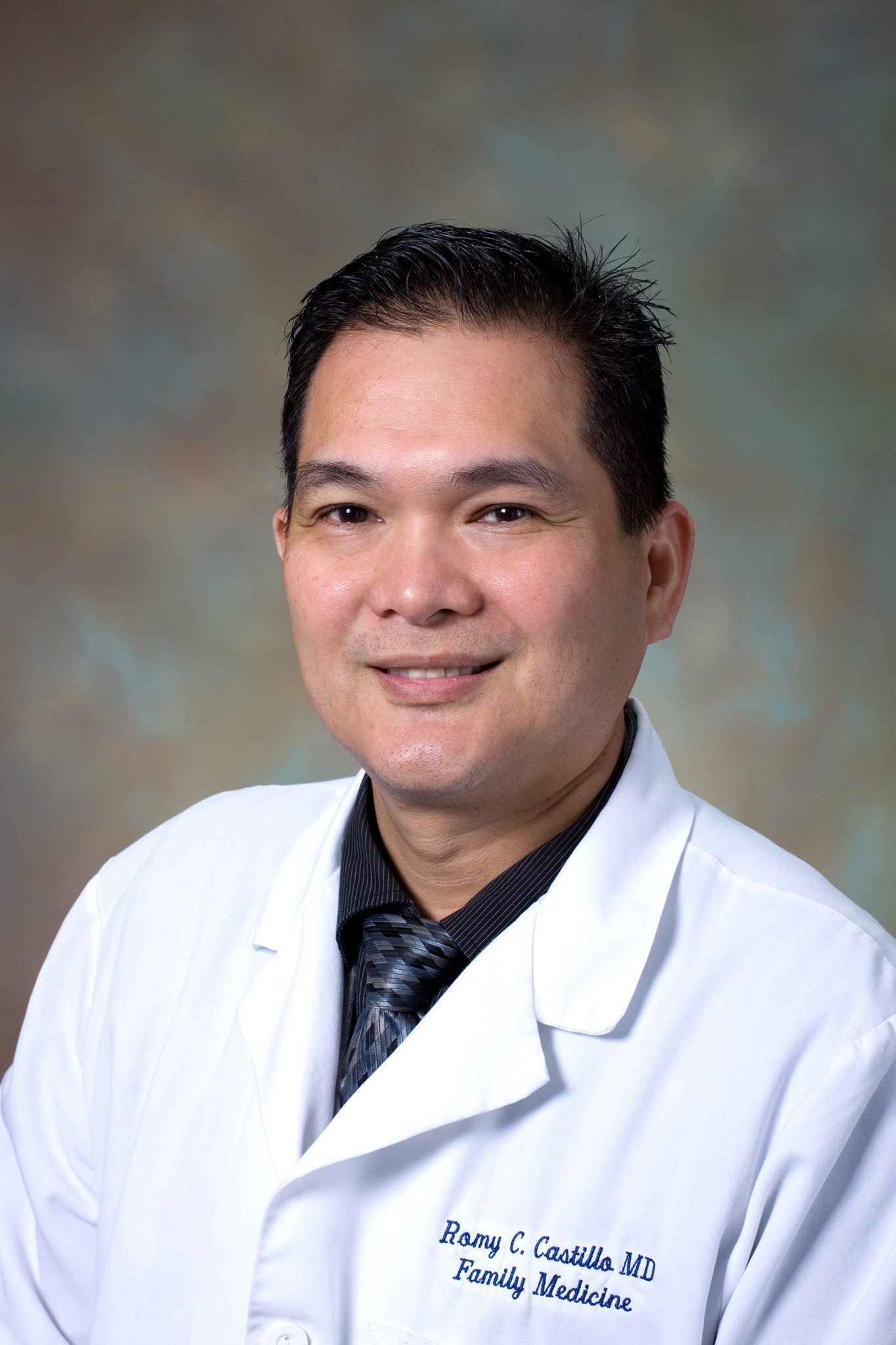 Smiling Asian doctor in white coat, dark tie, and short black hair.